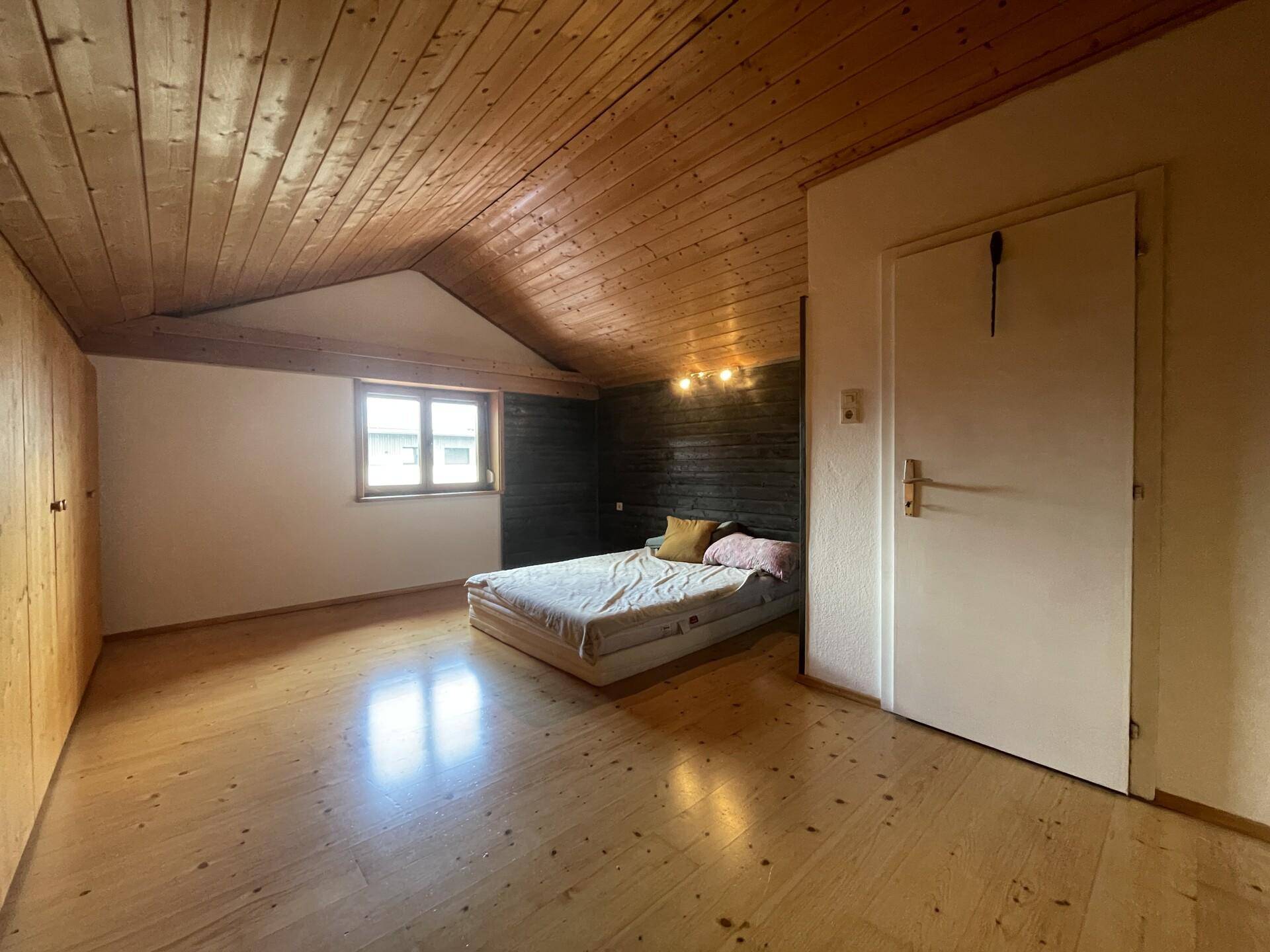 Helles Schlafzimmer im Dachgeschoss mit Holzboden, Holzdecke und schräger Wand.