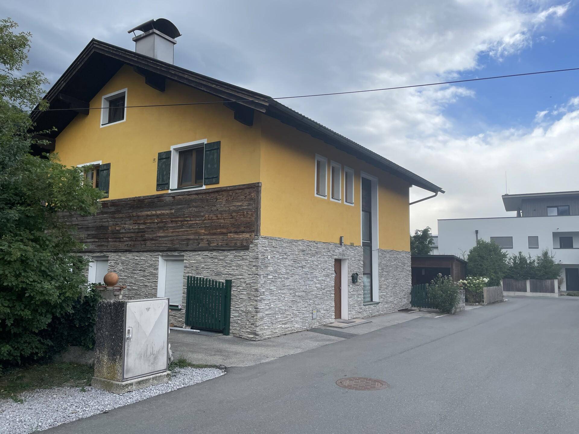 Freistehendes Haus mit gelber Fassade, Steinverkleidung und Satteldach.