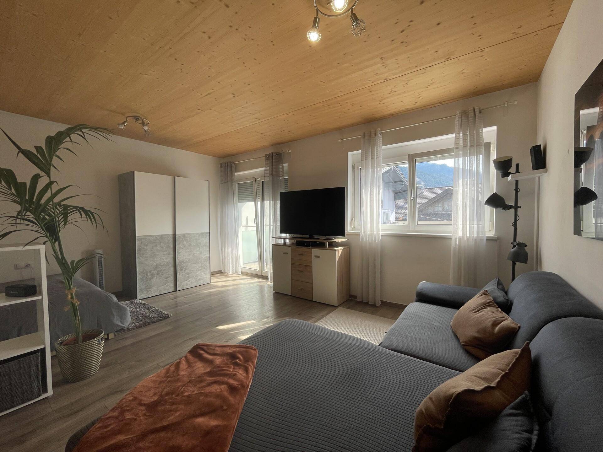 Gemütliches Wohnzimmer mit Holzbalkendecke, Sofa und Zugang zum Balkon.