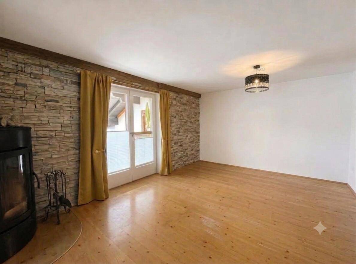 Geräumiges Wohnzimmer mit Holzboden, Steinwand und Kaminofen, bereit zur individuellen Einrichtung.