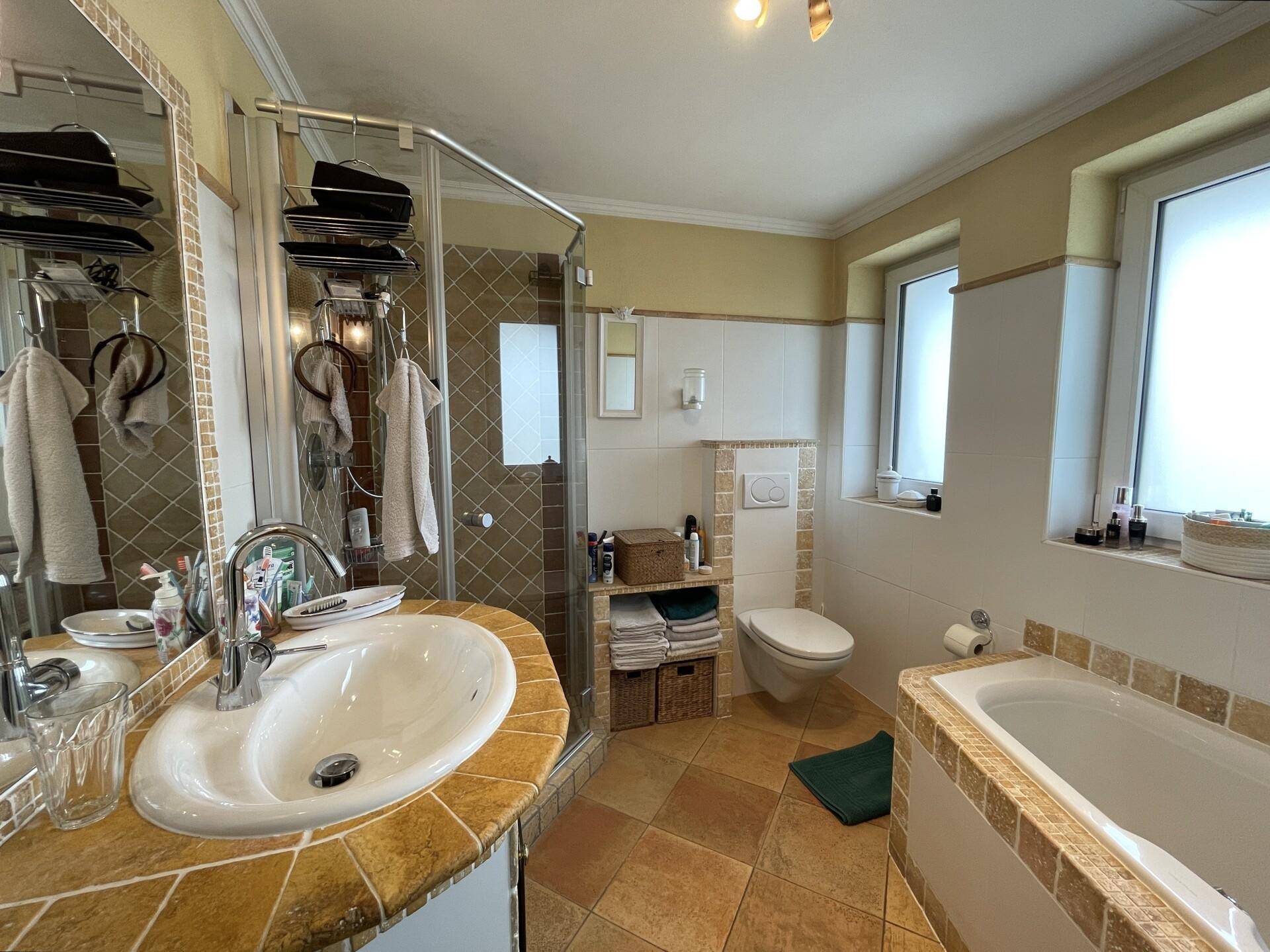 Funktionales Badezimmer im 80er-Jahre-Stil mit Dusche, Badewanne und zwei Fenstern.