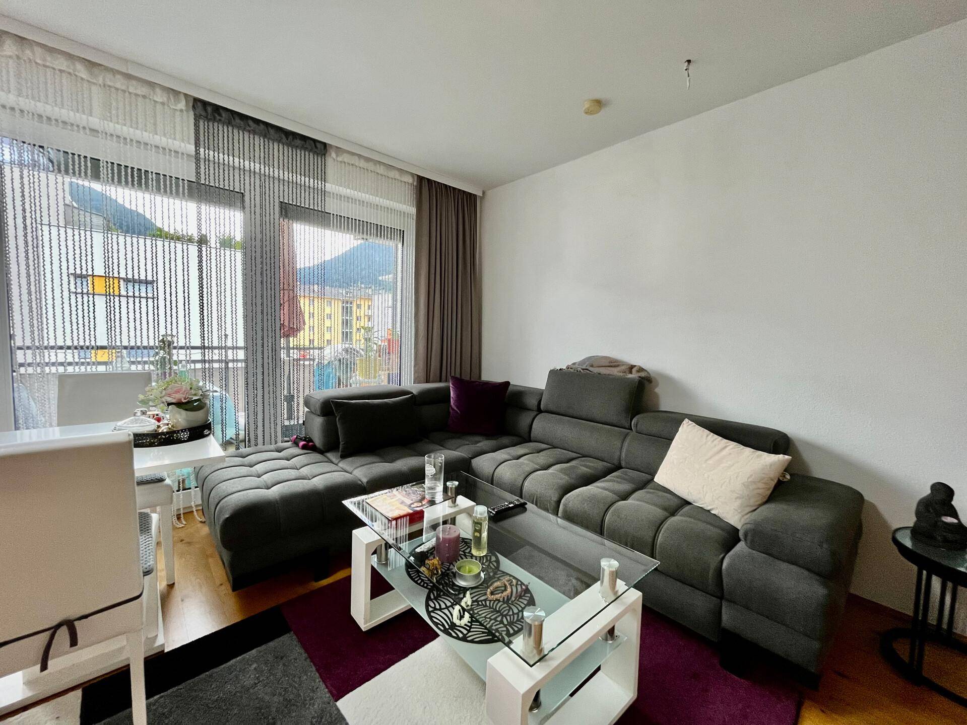 Gemütliches Wohnzimmer mit großem Ecksofa, Glastisch und Zugang zum Balkon.