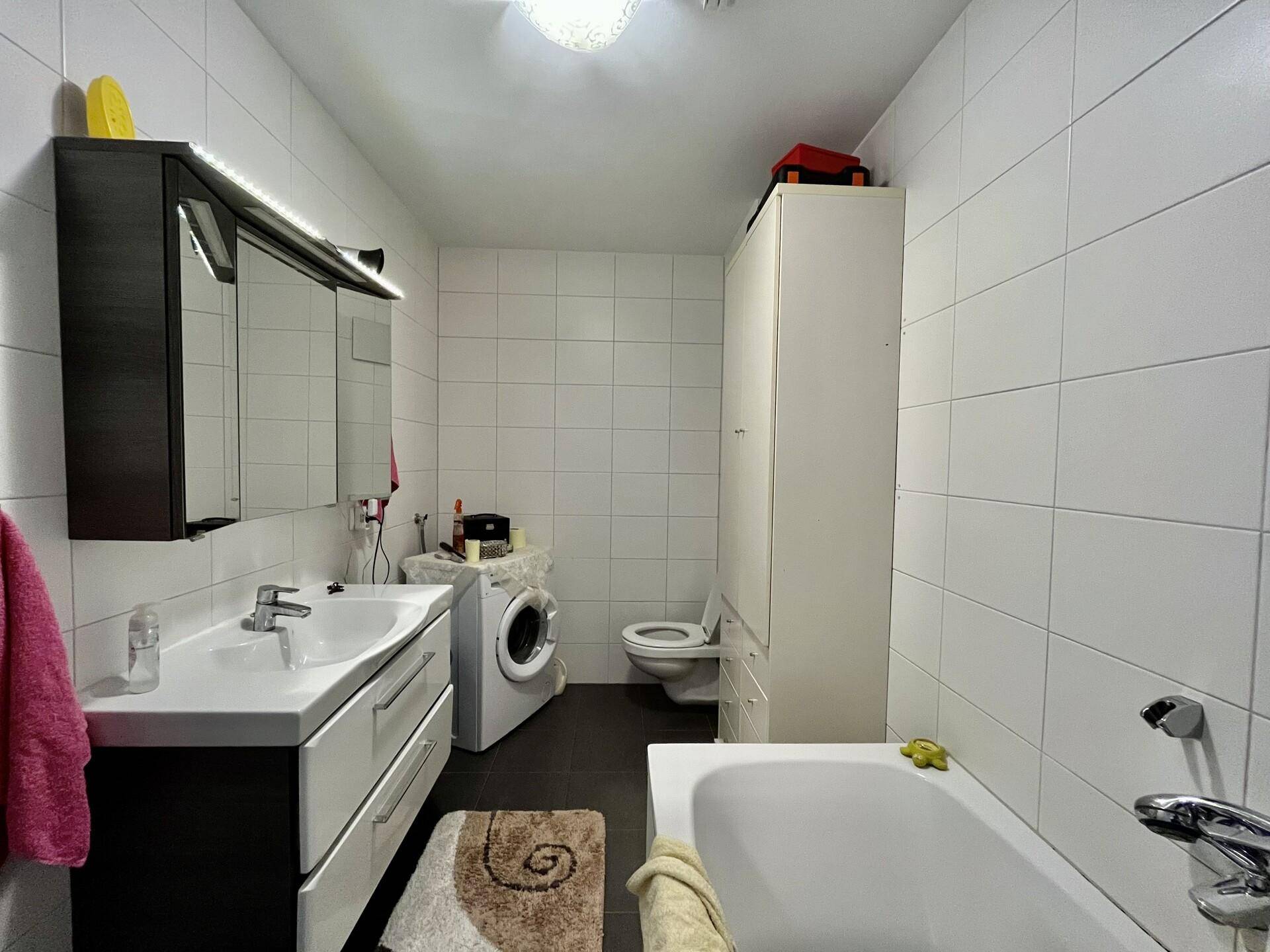 Modernes Badezimmer mit weißen Fliesen, Badewanne, Waschbecken und Waschmaschine.