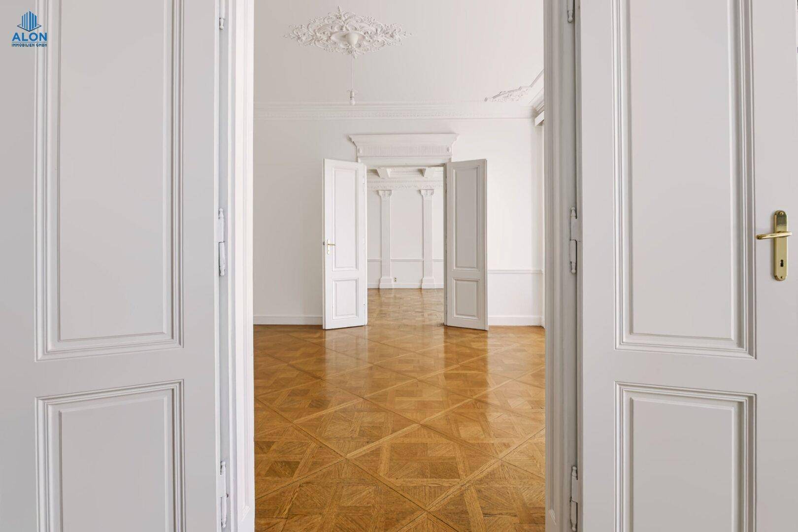 Blick durch offene Flügeltüren in einen weiteren Raum mit Parkettboden und eleganter Stuckdecke.
