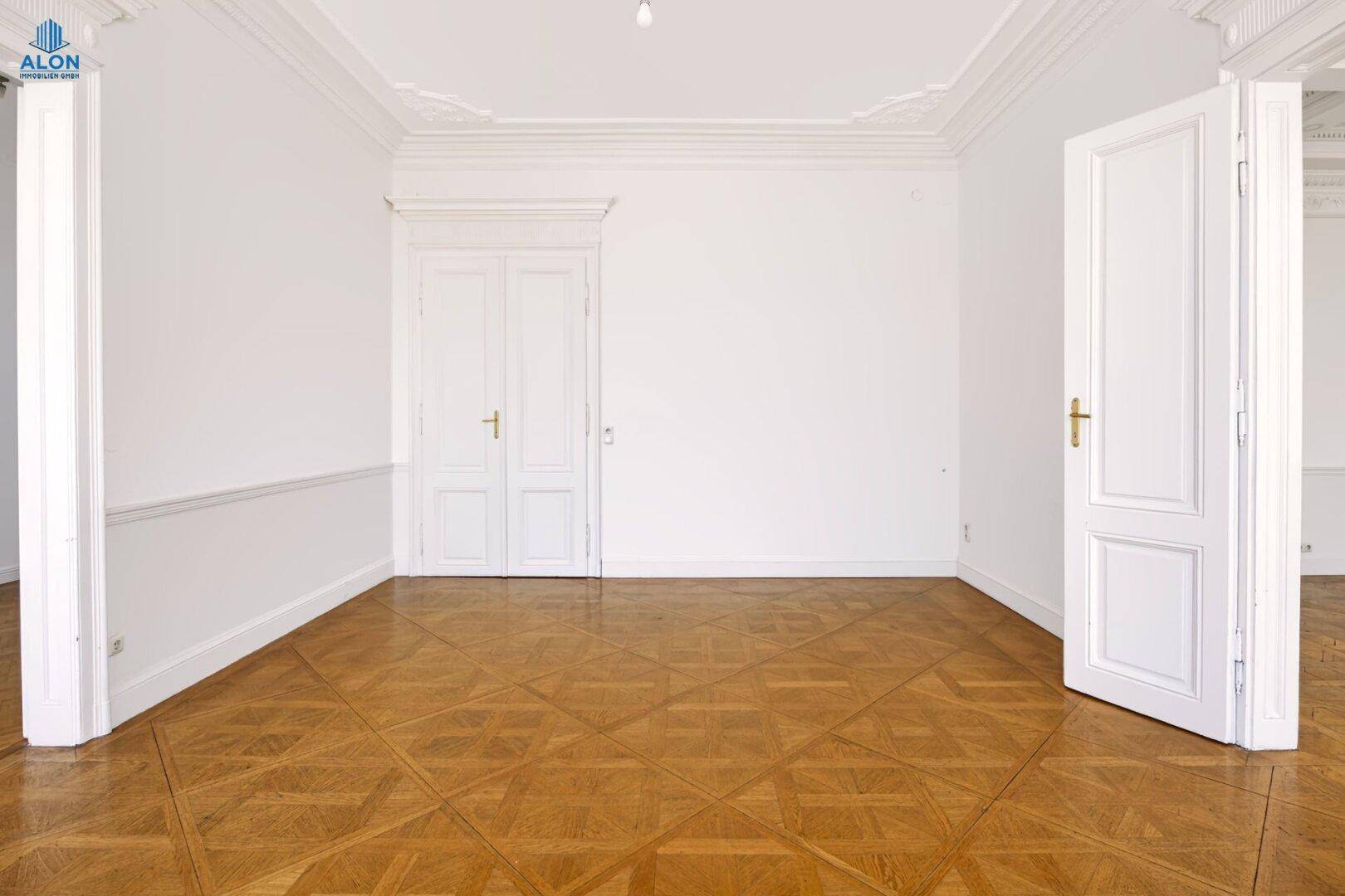 Helles Zimmer mit Parkettboden, hohen Decken und klassischen Flügeltüren, die den Altbaucharakter betonen.