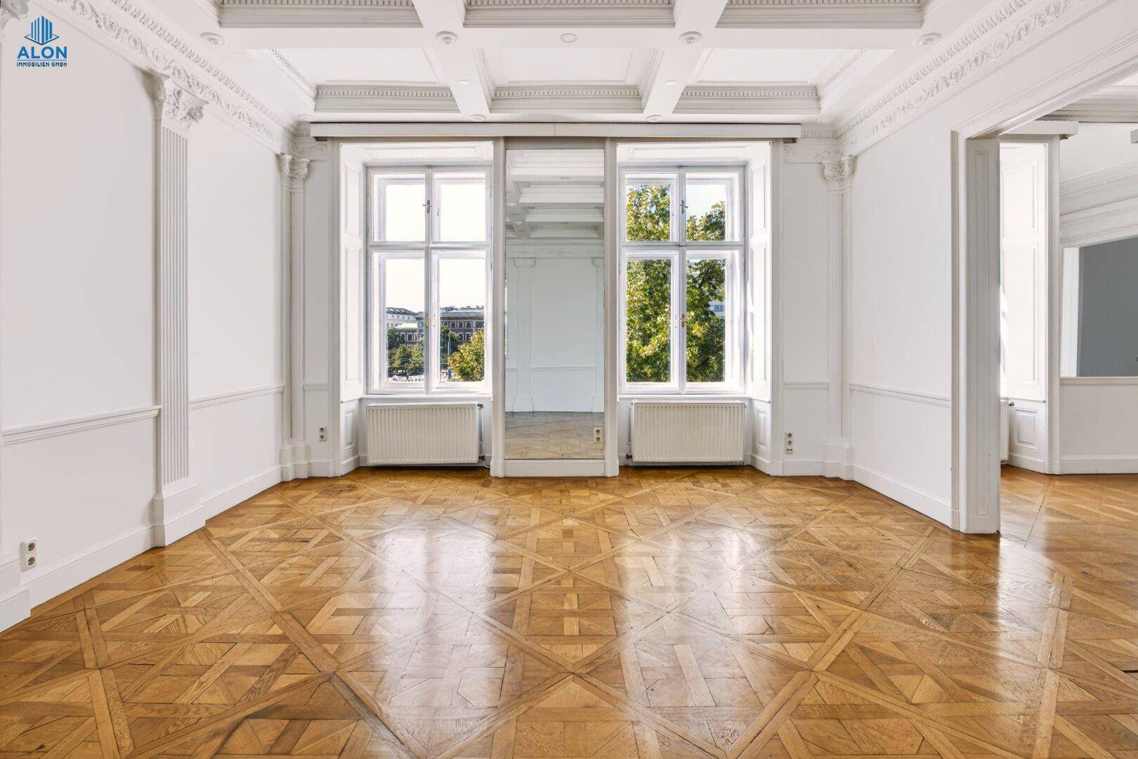 Geräumiges Zimmer mit aufwendiger Kassettendecke, Parkettboden und großen Fenstern, die viel Licht hereinlassen.