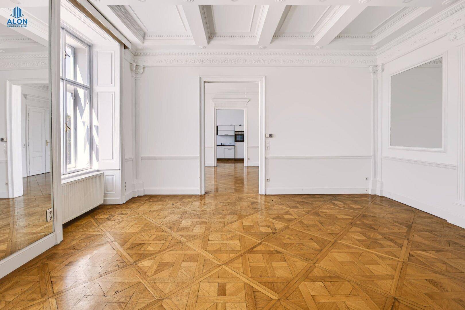 Heller Raum mit Parkettboden und Blick durch eine offene Tür in eine angrenzende, moderne Küche.