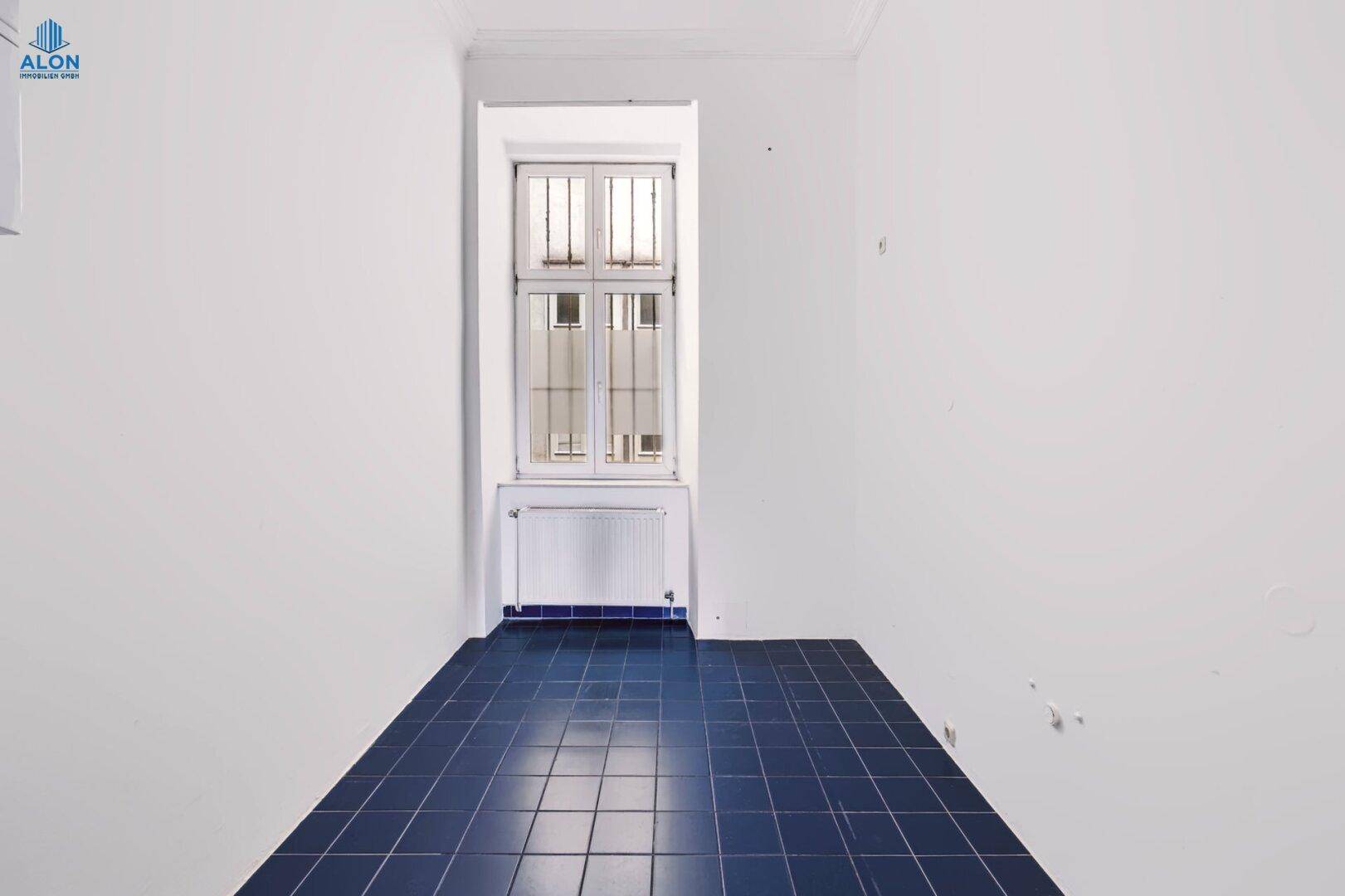Kleiner Raum mit blauen Fliesen, Fenster und Heizkörper, ideal als Abstellraum oder Waschküche.