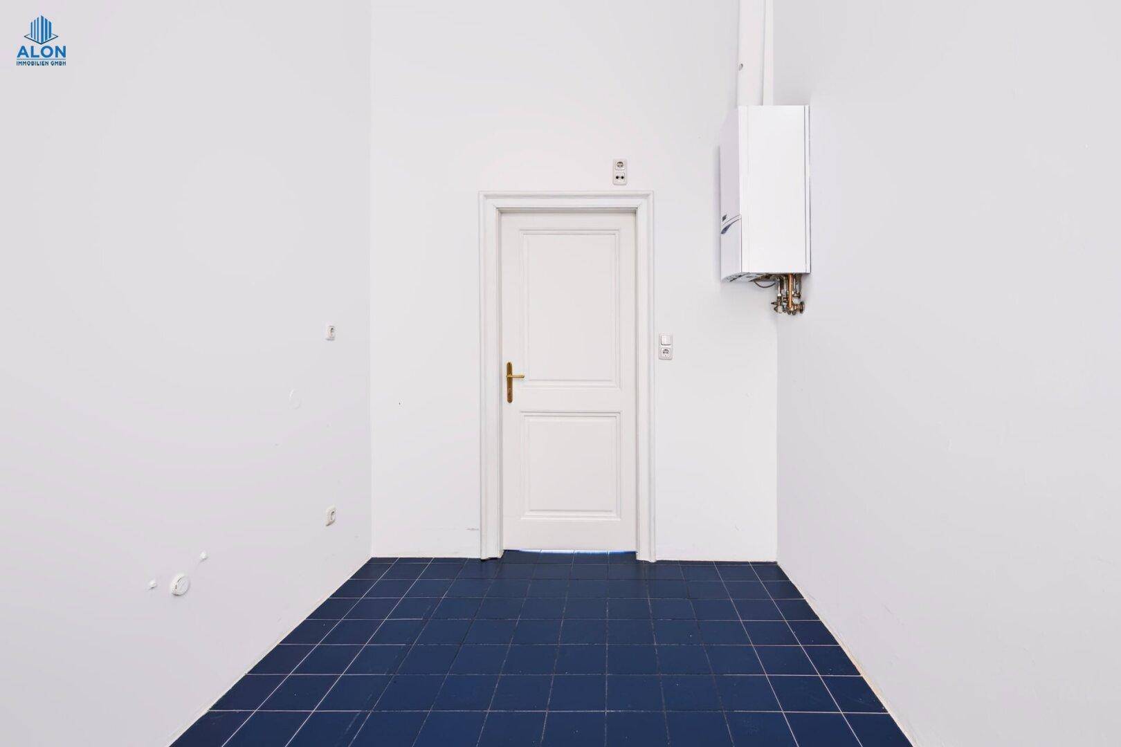 Kleiner Raum mit blauen Fliesen, weißer Tür und Gastherme an der Wand, funktional und sauber.