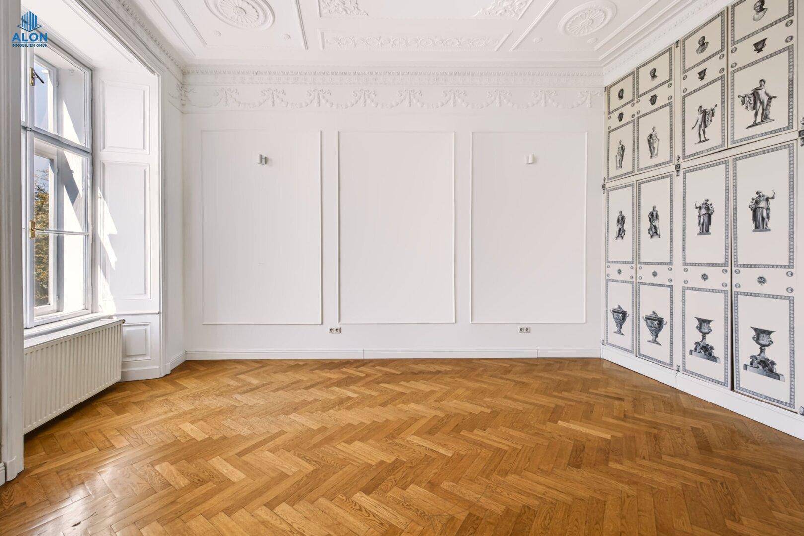 Großes Zimmer mit Fischgrätparkett, hohen Decken und dekorativen Wandpaneelen, die eine elegante Atmosphäre schaffen.