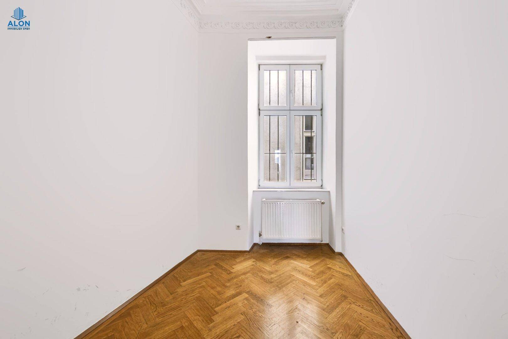Helles Schlafzimmer mit Fischgrätparkett, hohen Decken und Fenster mit Gitter, das Sicherheit bietet.