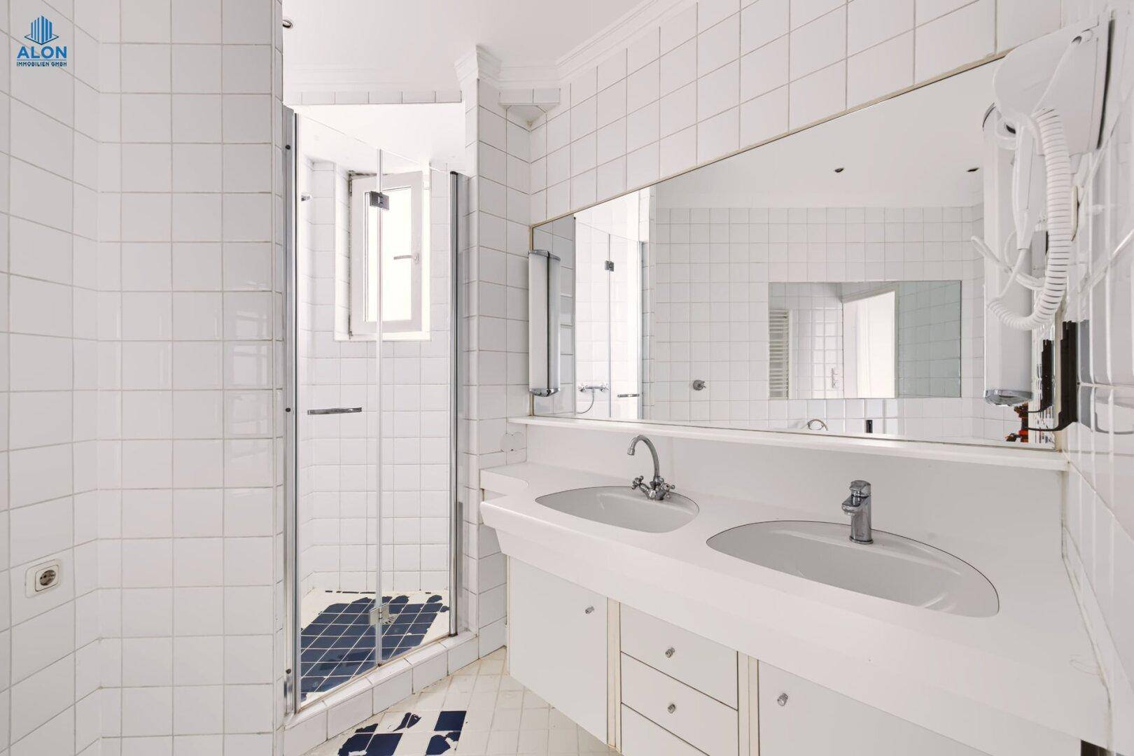 Modernes Badezimmer mit Doppelwaschbecken, großem Spiegel und Duschkabine, alles in Weiß gehalten.
