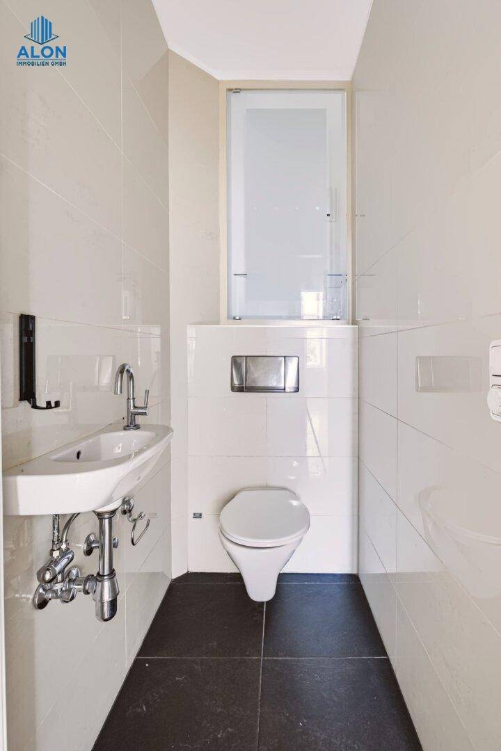 Modernes Gäste-WC mit wandhängender Toilette, kleinem Waschbecken und dunklem Boden, sehr sauber.