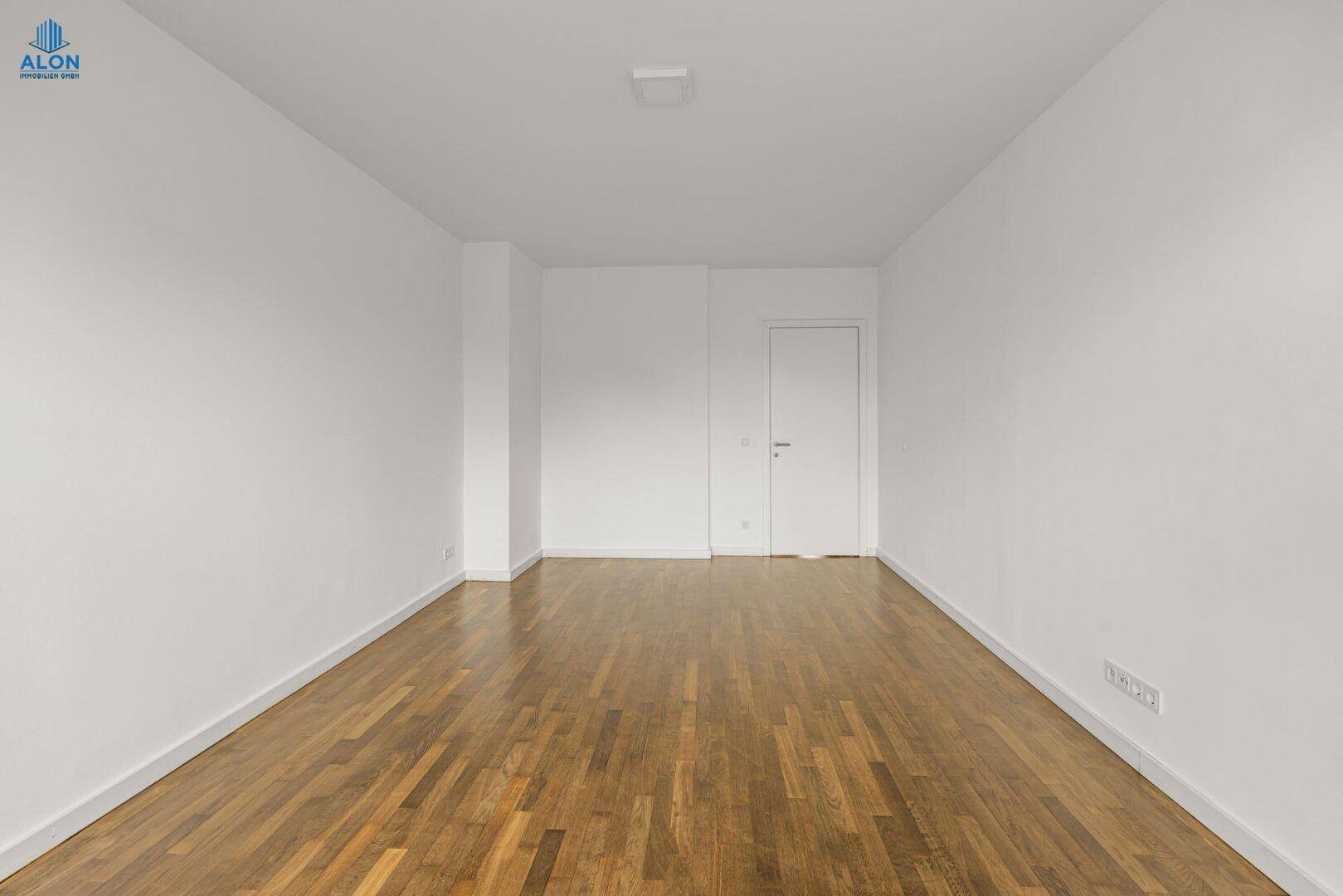 Helles, leeres Zimmer mit Holzboden und schlichten weißen Wänden, bereit zur individuellen Gestaltung.