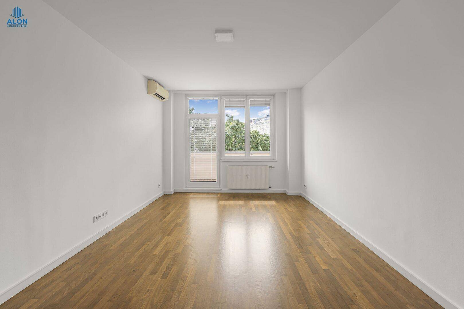 Leeres Zimmer mit Parkettboden und Zugang zu einem Balkon, ideal als Schlaf- oder Arbeitszimmer.