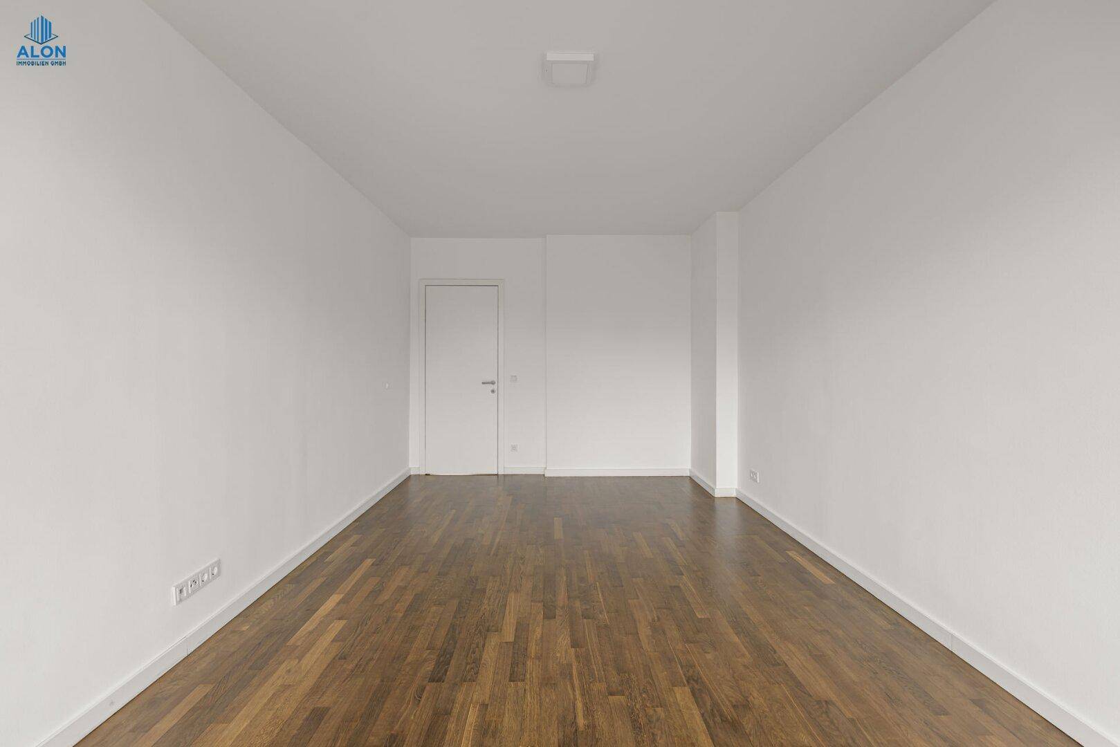 Leeres Zimmer mit glänzendem Parkettboden und schlichten weißen Wänden, vielseitig nutzbar.
