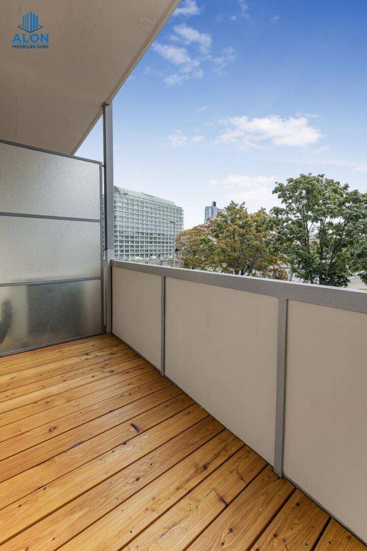 Heller Balkon mit Holzdielen und seitlichem Blick auf die umliegende Stadtbebauung und Bäume.
