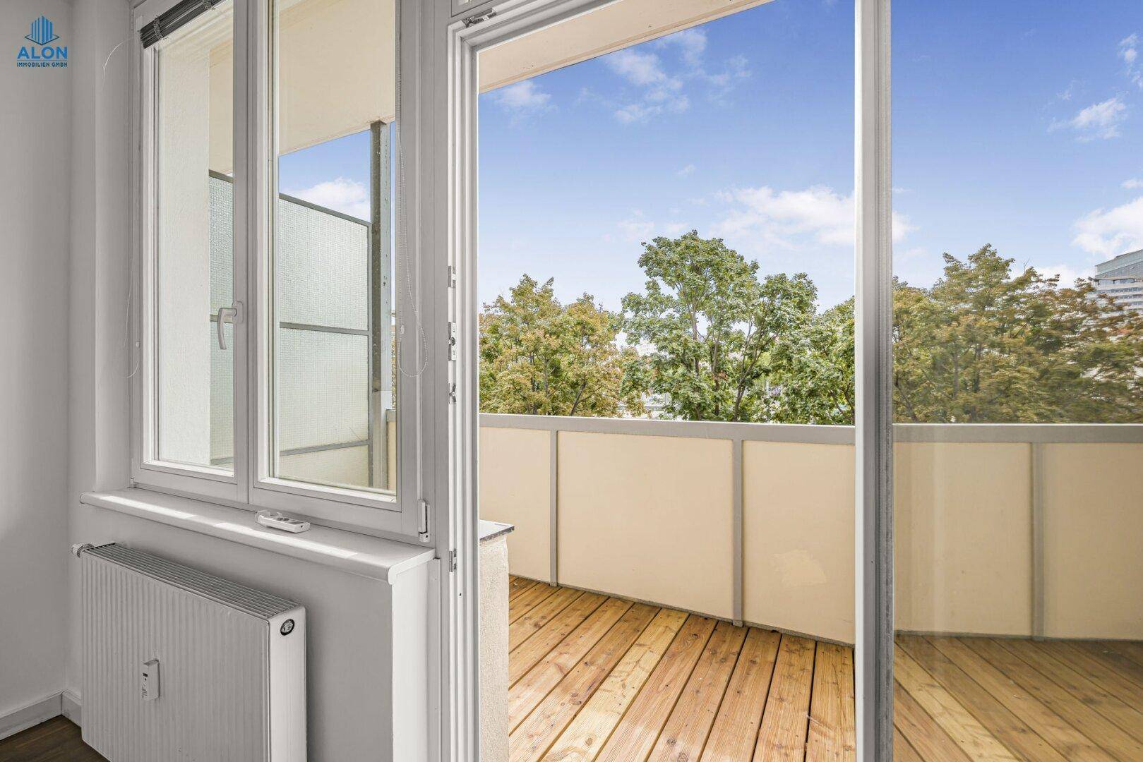Blick vom Zimmer auf den Balkon mit Holzdielen und Stadtansicht, ideal für entspannte Stunden.