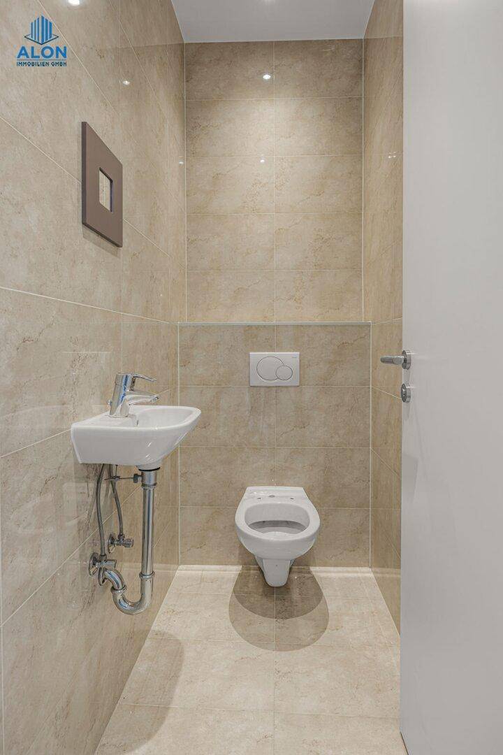 Gäste-WC mit wandhängendem WC, kleinem Waschbecken und hellen Fliesen, funktional und sauber.