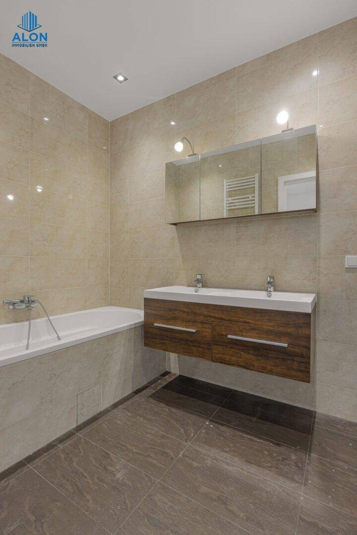 Elegantes Badezimmer mit Badewanne, Doppelwaschbecken und großformatigen Fliesen, gut beleuchtet.