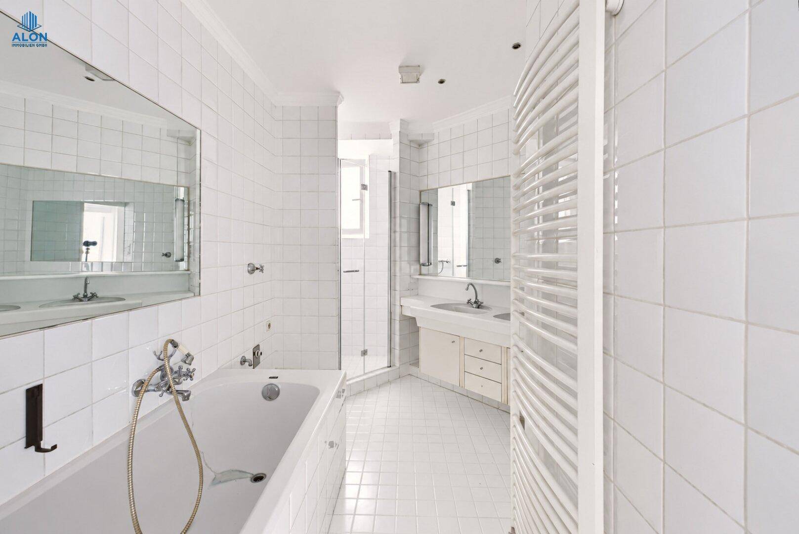 Helles Badezimmer mit weißen Fliesen, Badewanne, Duschkabine und beheiztem Handtuchhalter.