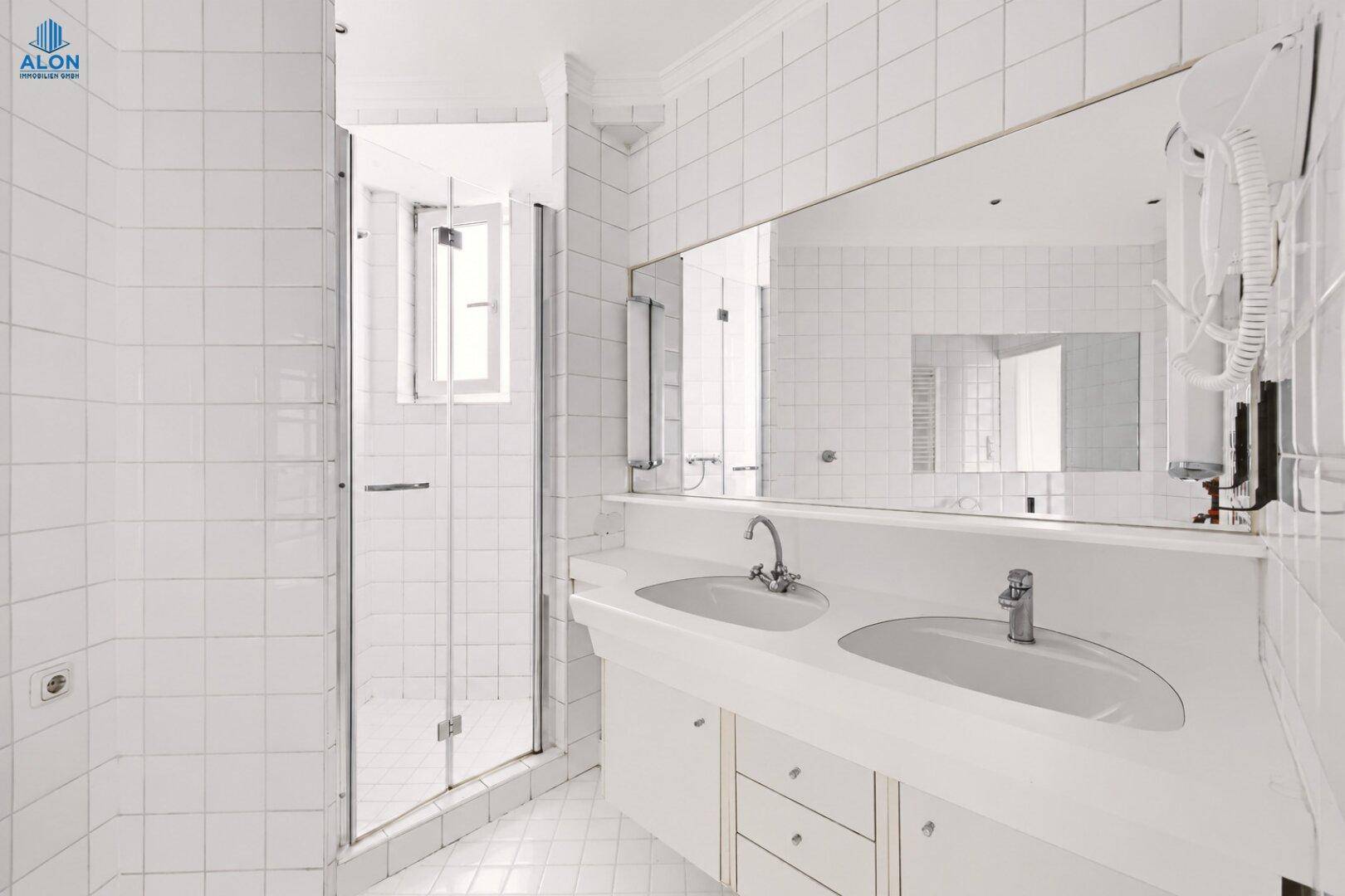 Funktionales Badezimmer mit Doppelwaschbecken, großer Spiegelfläche und Duschkabine.