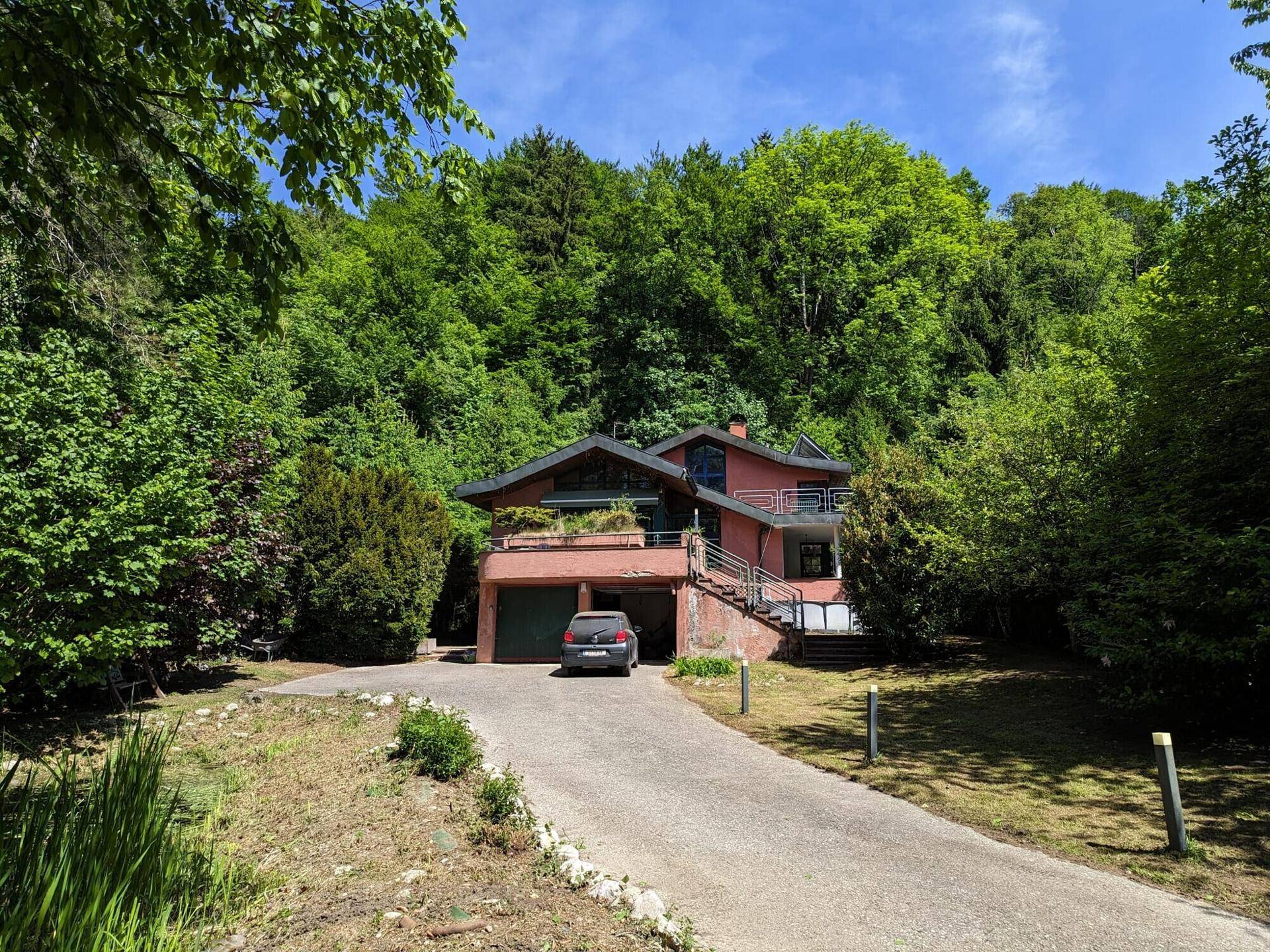 Ansicht des Hauses mit integrierter Garage und Zufahrt, umgeben von dichtem Grün.