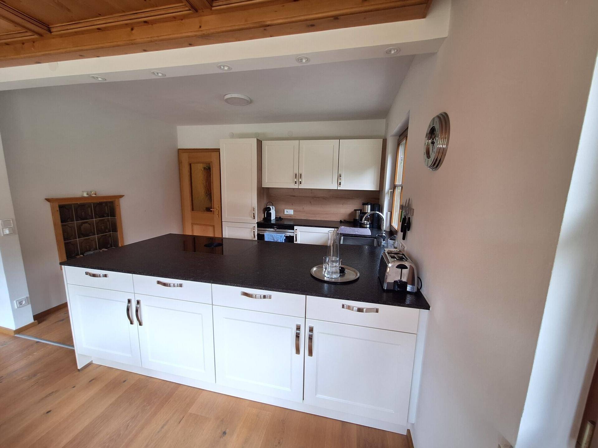 Moderne Küche mit Kücheninsel, weißen Schränken, dunkler Arbeitsplatte und Holzboden.