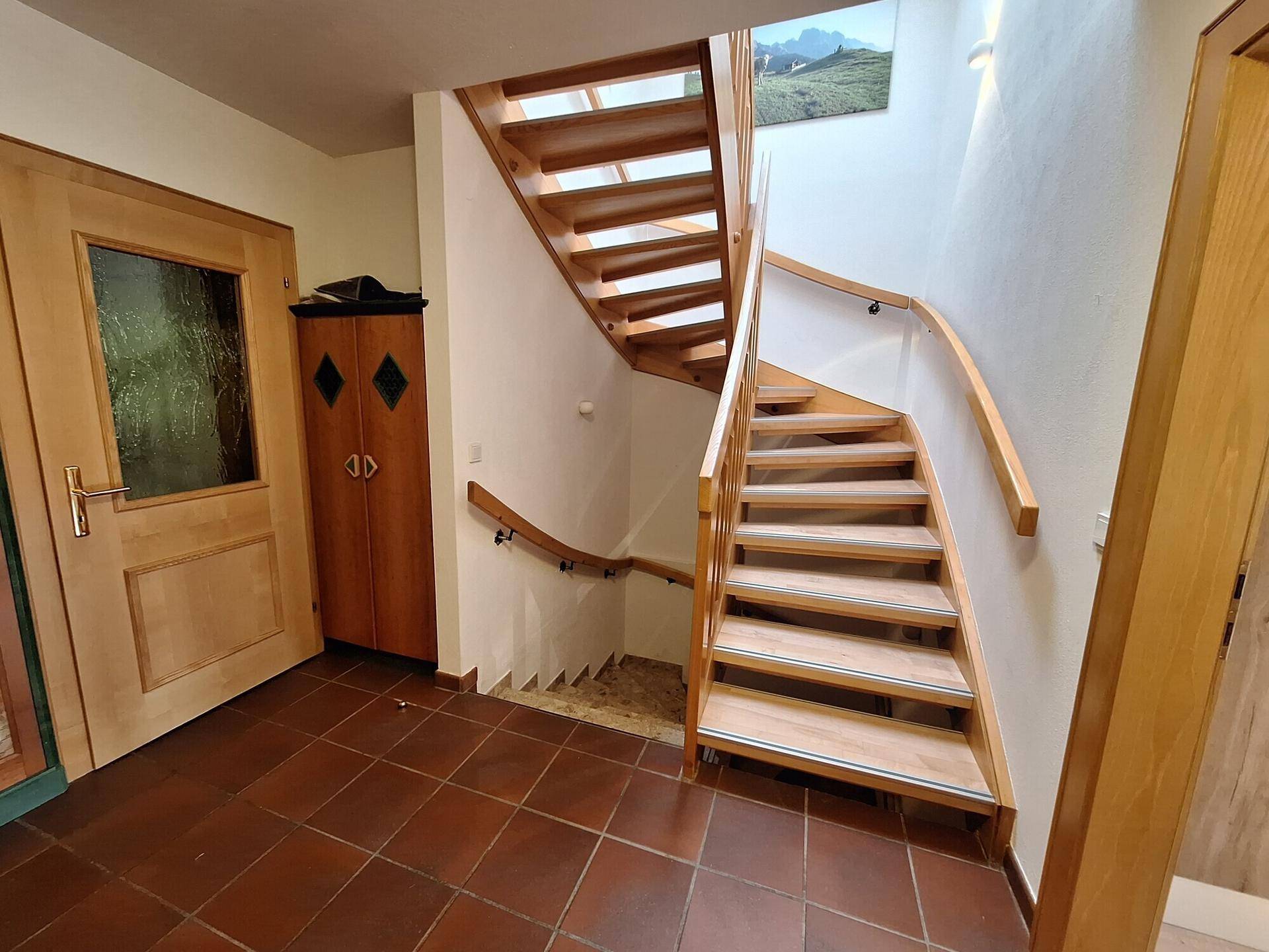 Heller Eingangsbereich mit Holztreppe, Fliesenboden und Zugang zu den oberen Etagen.