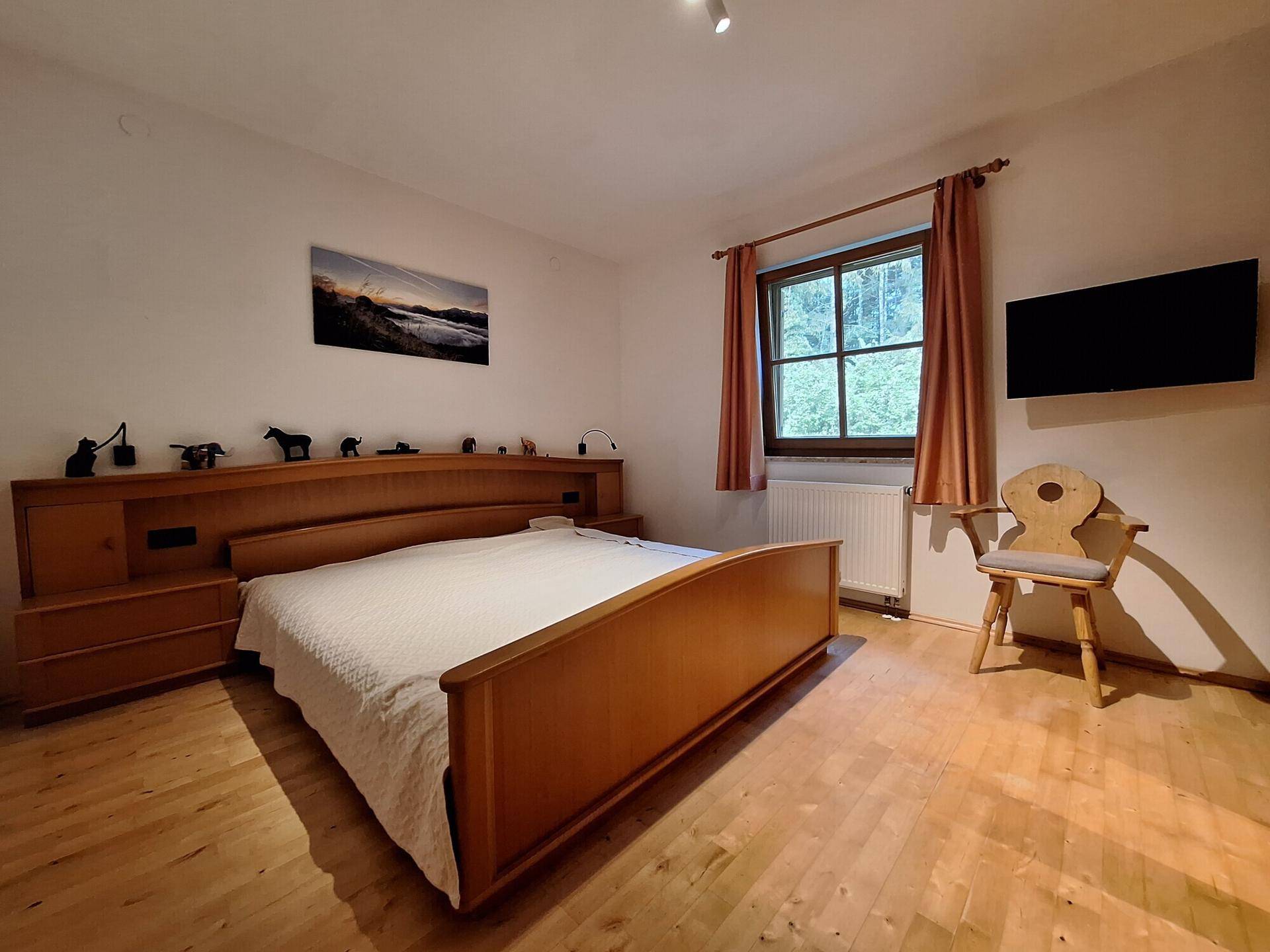 Komfortables Schlafzimmer mit Holzbett, Holzboden und Blick auf die umliegende Natur.
