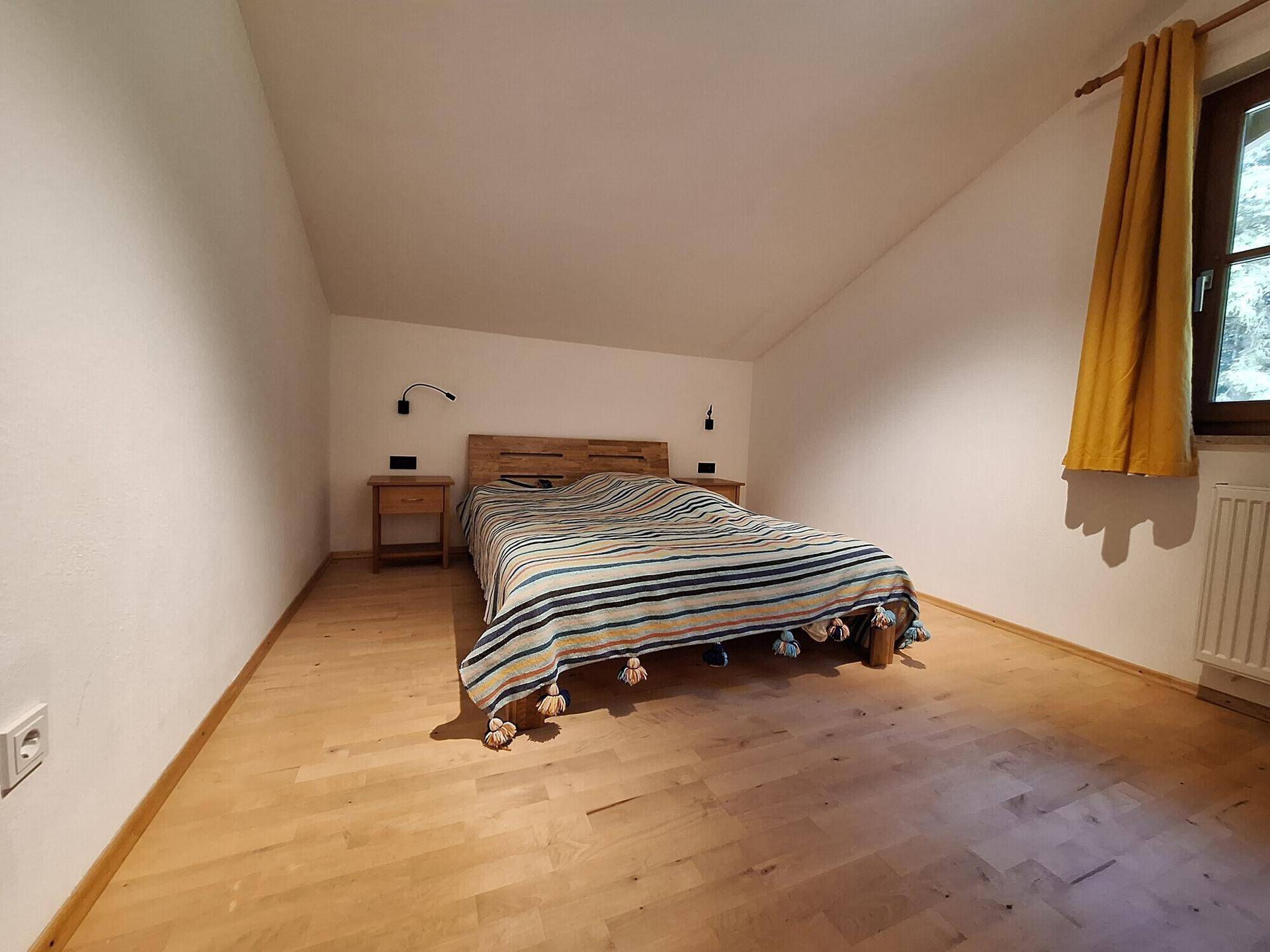 Gemütliches Schlafzimmer mit Holzbett, Holzboden und einem Fenster mit Blick ins Grüne.