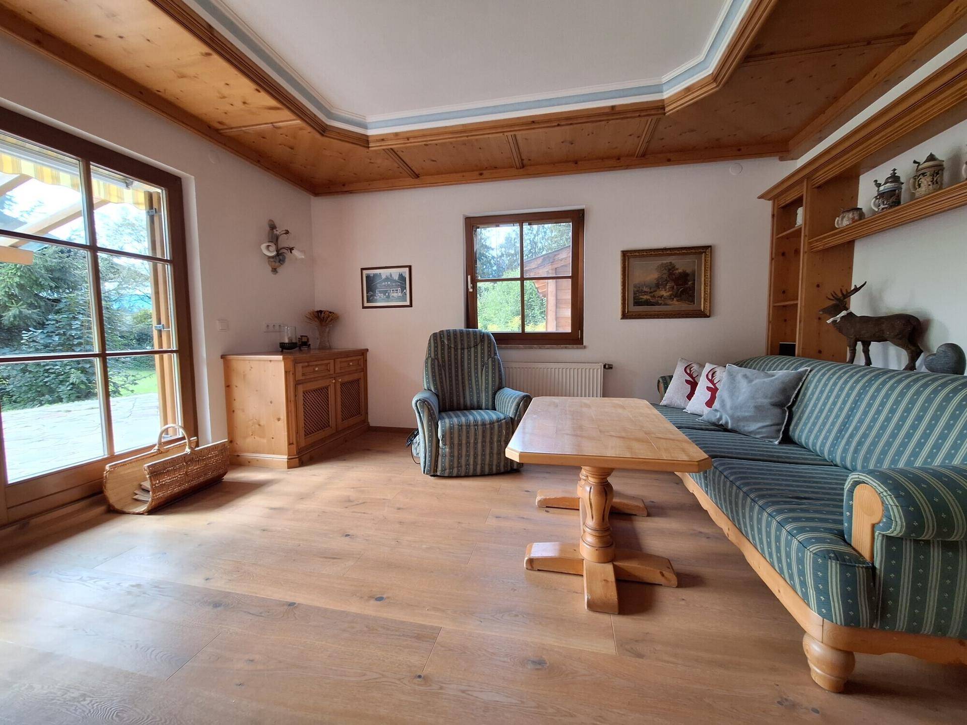 Gemütliches Wohnzimmer im alpenländischen Stil mit Holzbalkendecke, Parkettboden und Zugang zur Terrasse.