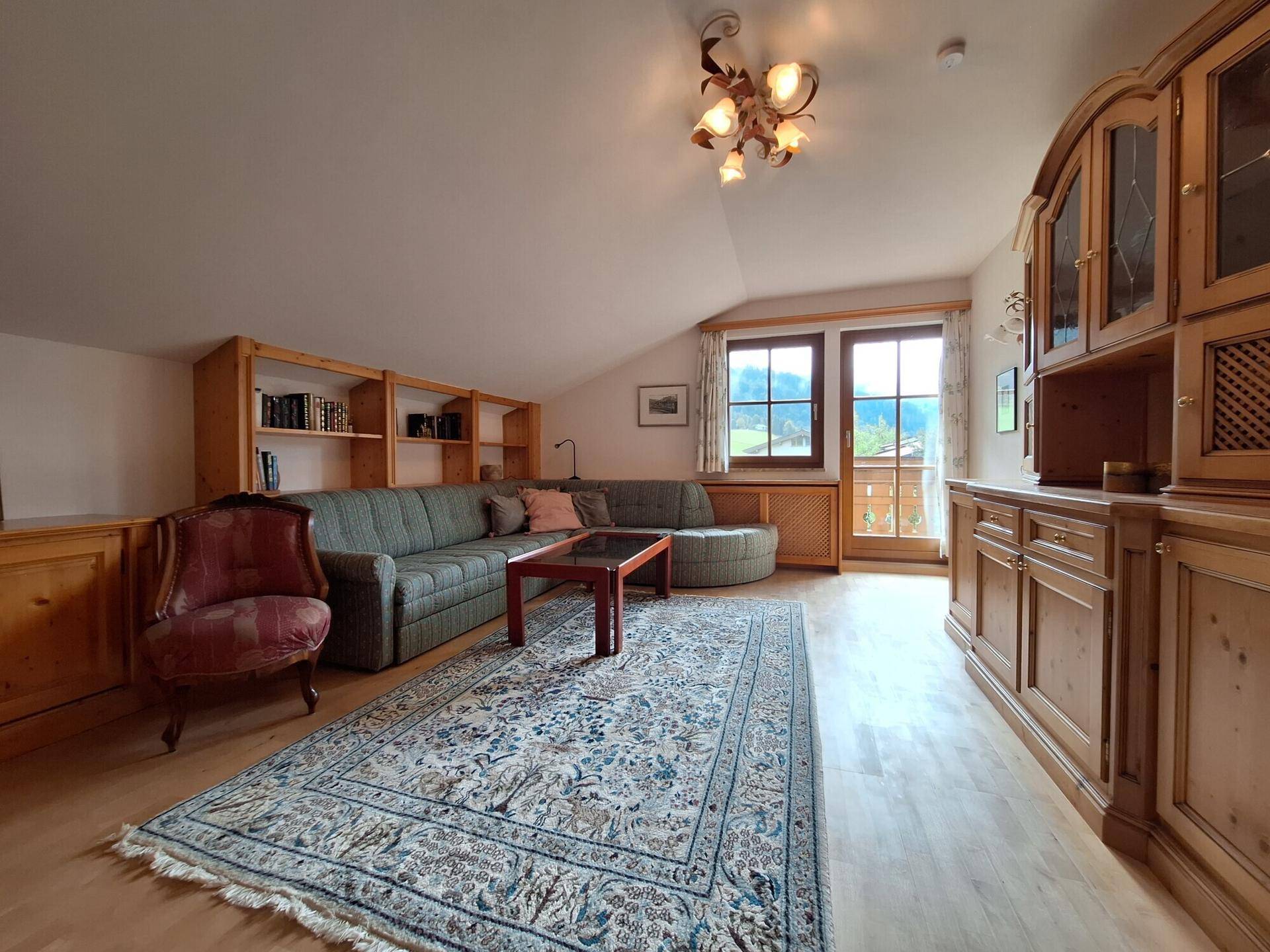 Geräumiges Wohnzimmer im Dachgeschoss mit Holzeinbauten, Teppich und Balkonzugang mit Bergblick.