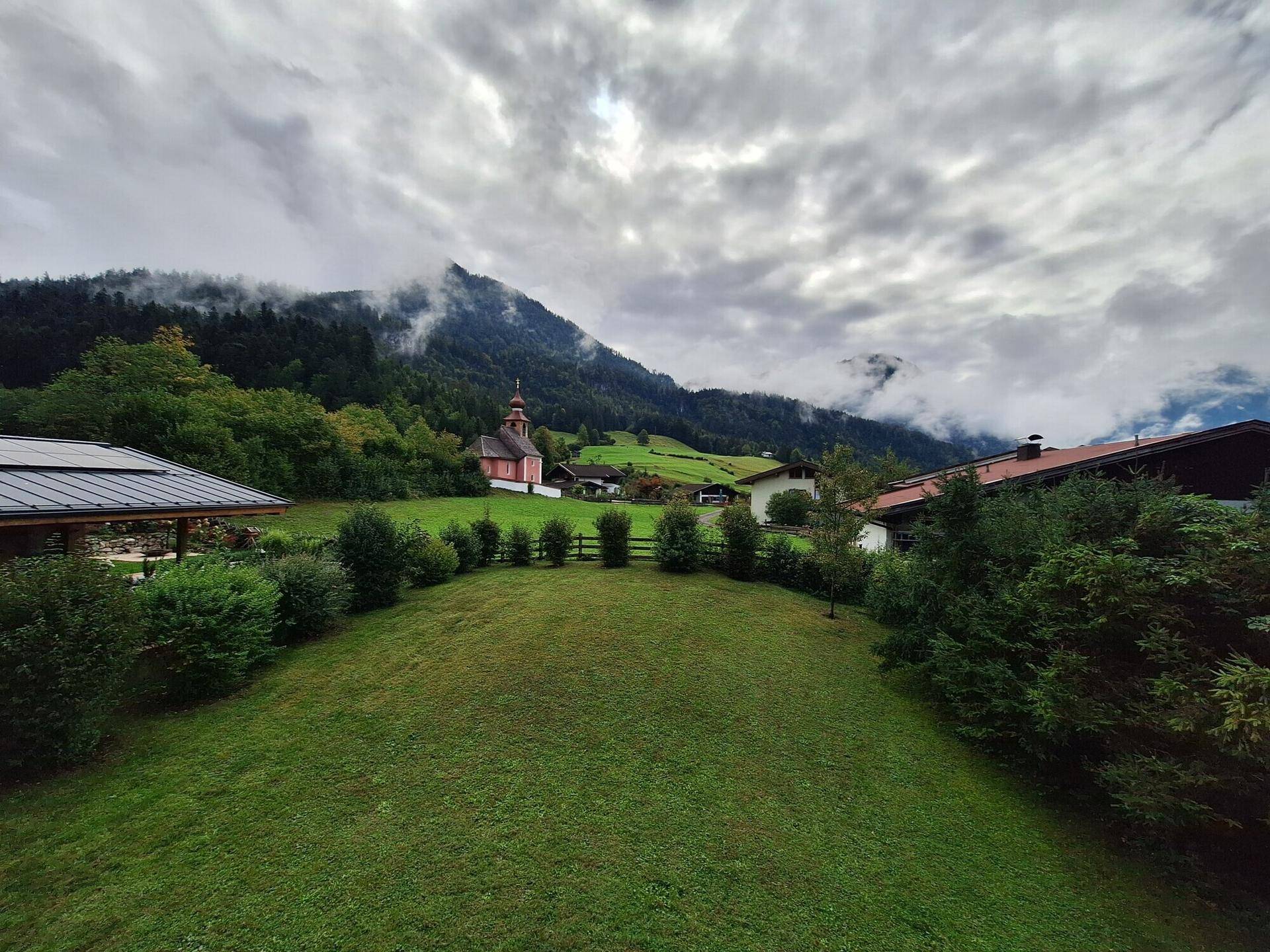 Malerische Landschaft mit grünen Hügeln, Bergen und einem kleinen Kirchlein in der Ferne.