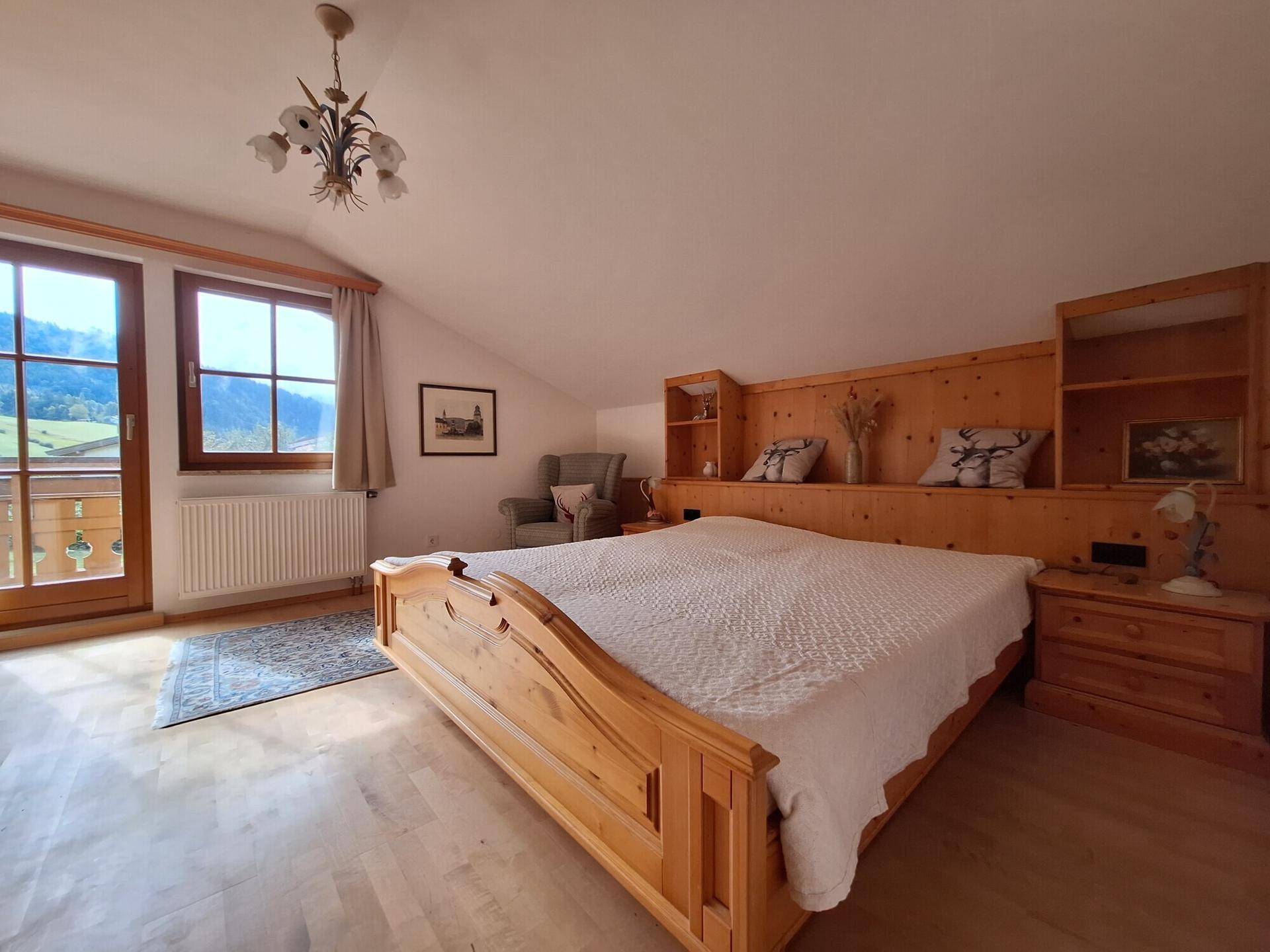 Helles Schlafzimmer im Dachgeschoss mit Holzbett, Einbauschränken und Balkonzugang mit Bergblick.