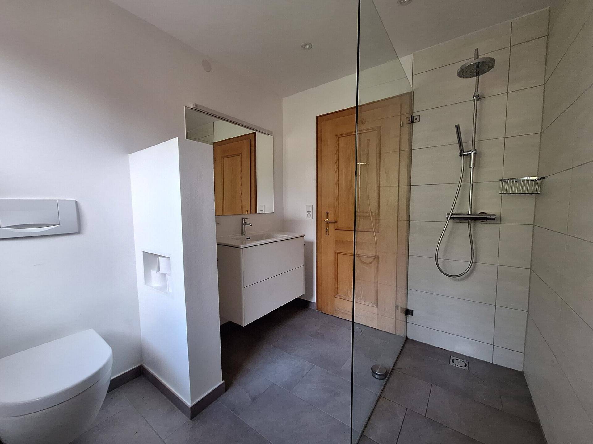 Modernes Badezimmer mit begehbarer Dusche, Wand-WC und großformatigen Fliesen in neutralen Farben.