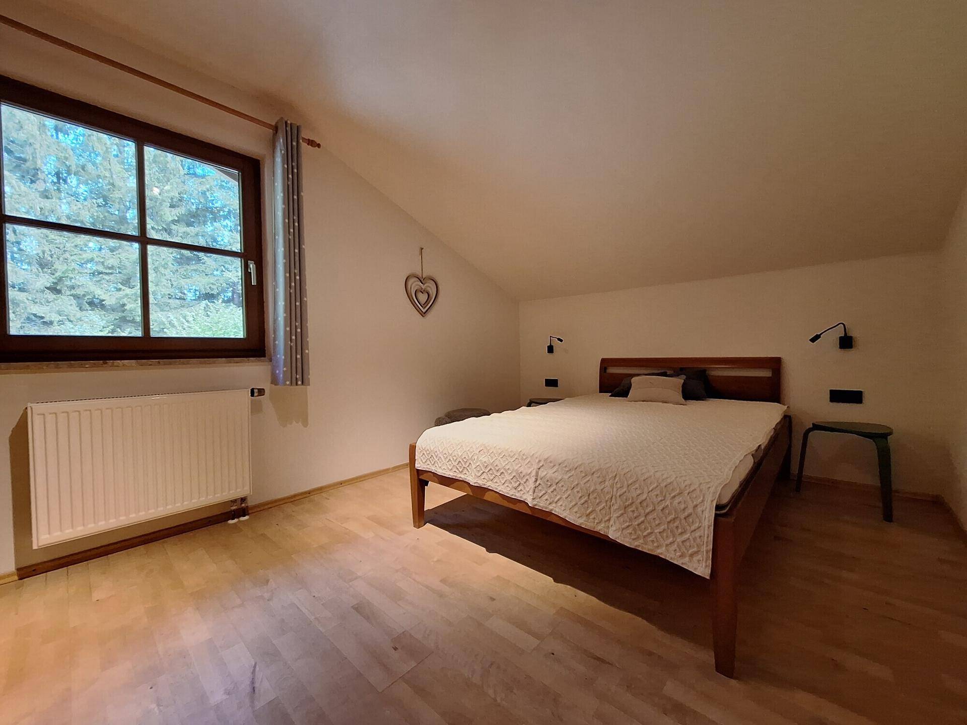 Ruhiges Schlafzimmer im Dachgeschoss mit Holzbett, Holzboden und Fenster mit Blick ins Grüne.