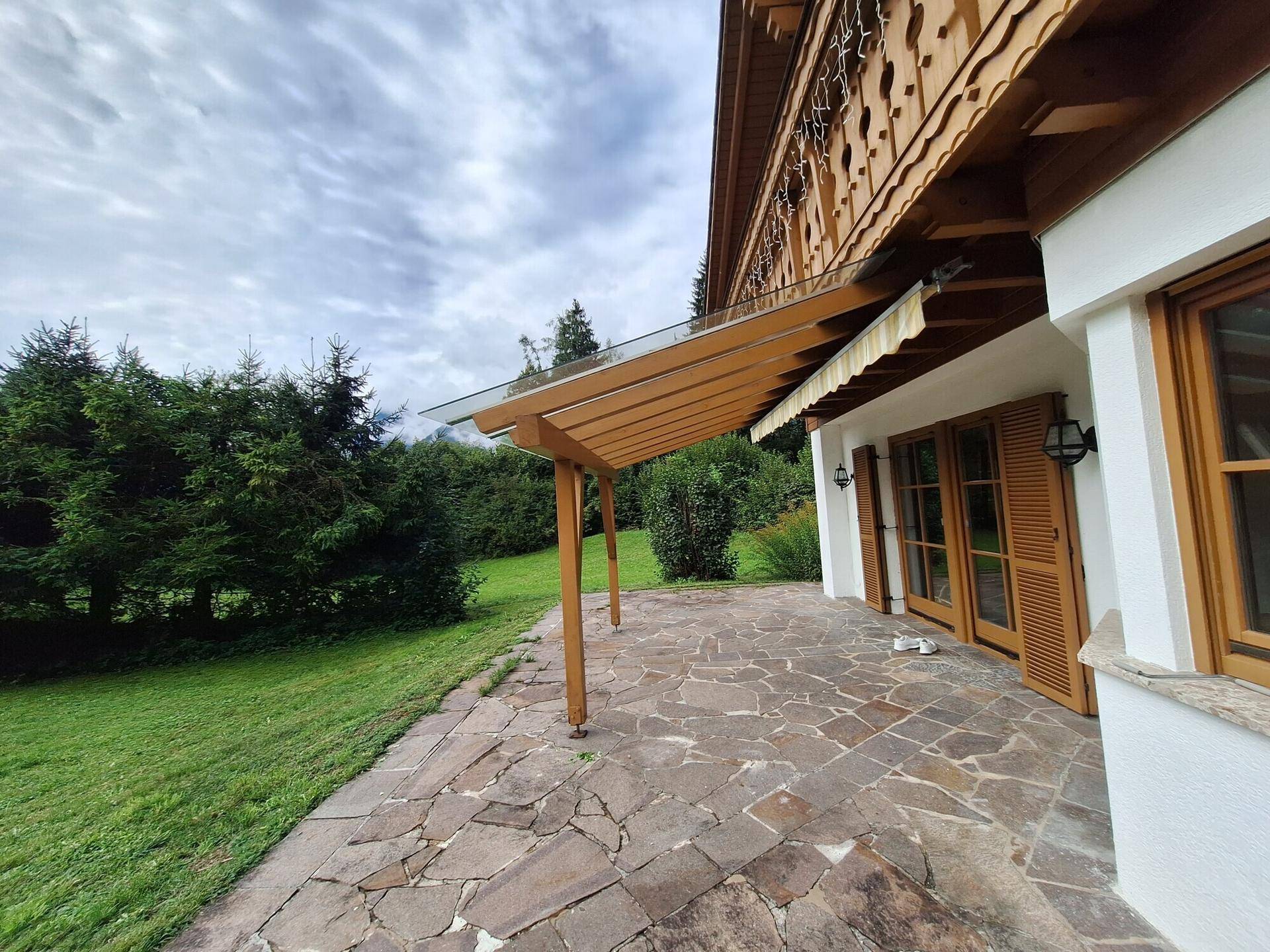 Überdachte Terrasse mit Steinplattenboden und Zugang zum Garten, ideal für entspannte Stunden im Freien.