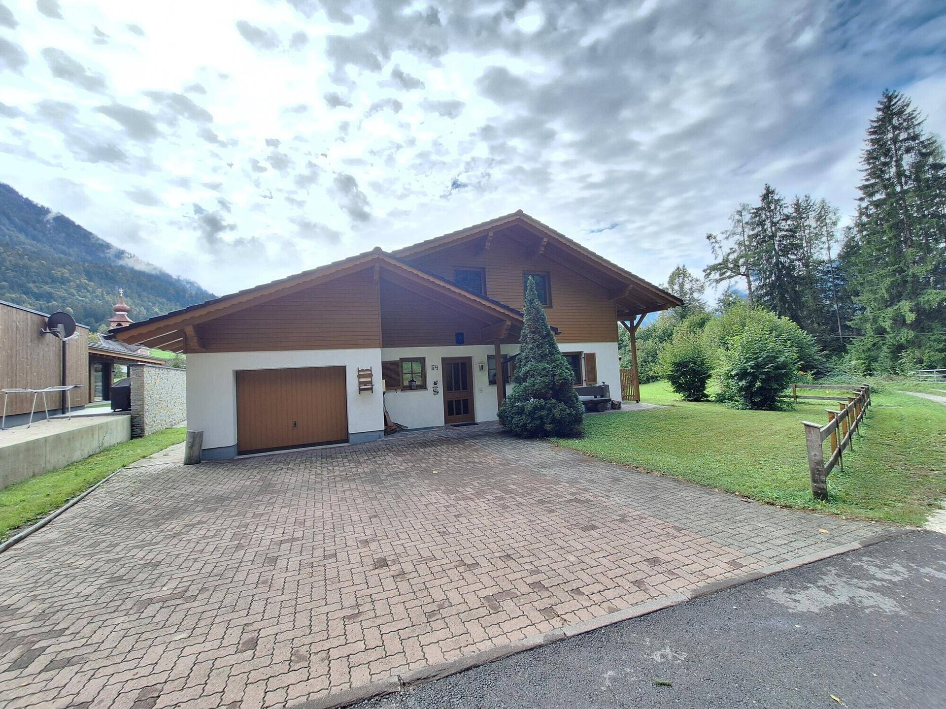 Traditionelles Haus mit integrierter Garage, gepflasterter Auffahrt und umgebender Natur.