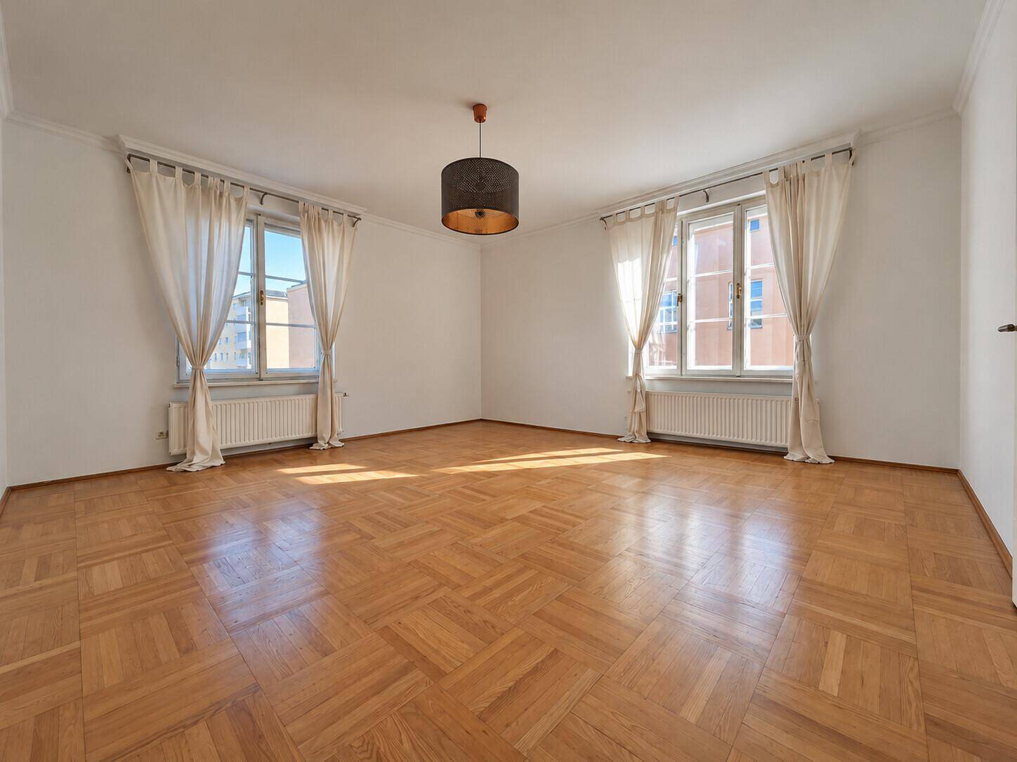 Geräumiges Wohnzimmer mit klassischem Parkettboden und viel Tageslicht durch die Fenster.