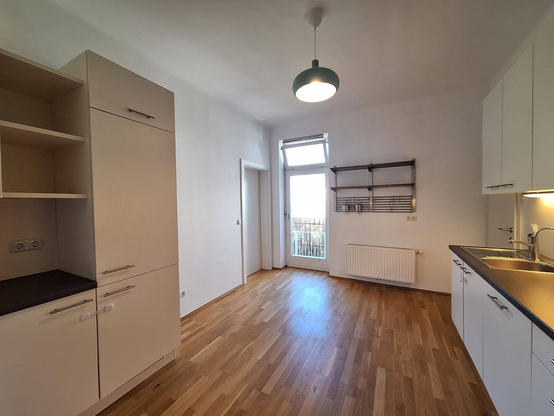 Helle Küche mit Zugang zu einem französischen Balkon und Holzparkett, mit viel Stauraum.