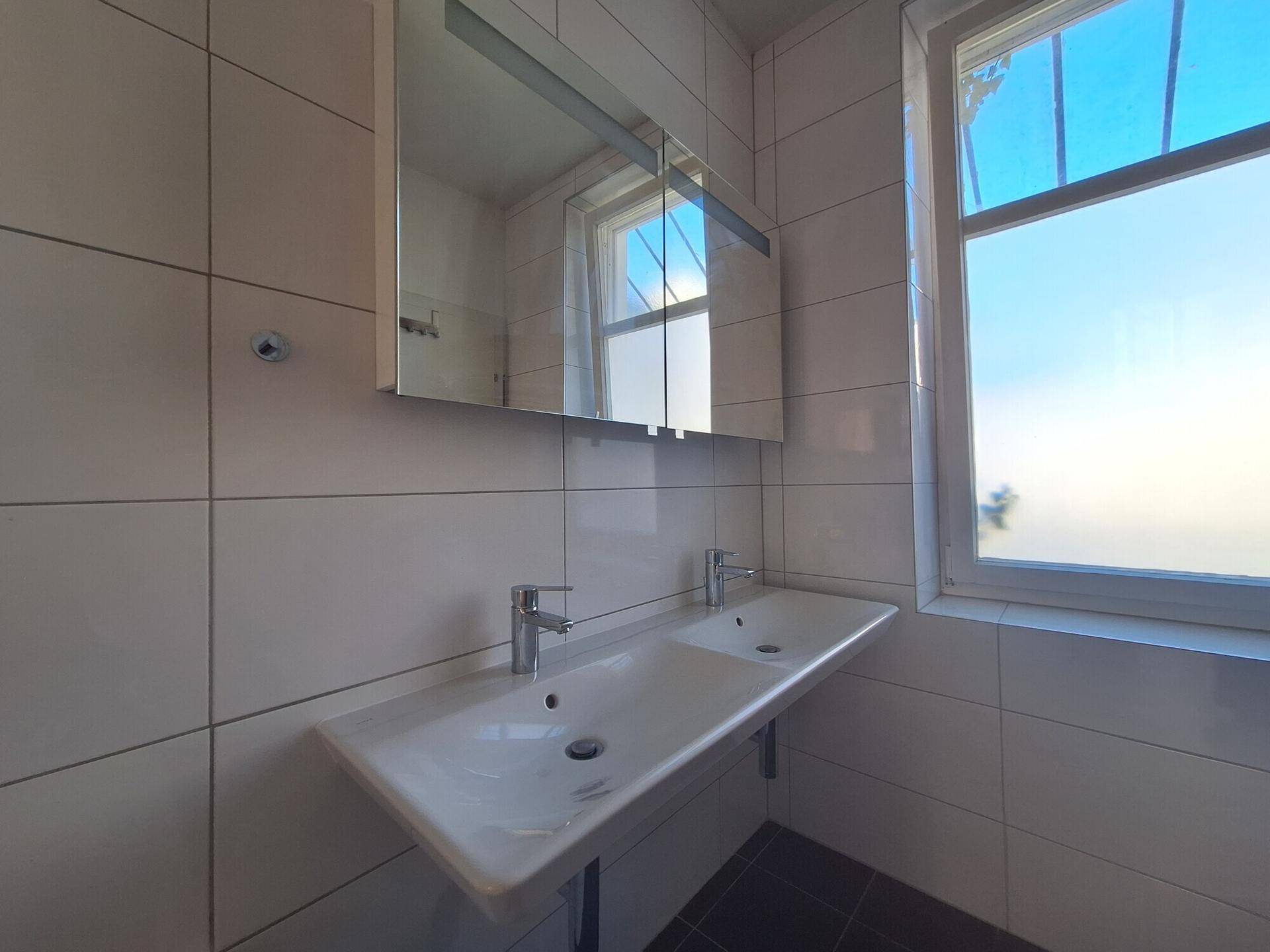 Helles Badezimmer mit Doppelwaschbecken, Spiegelschrank und Fenster für natürliche Belüftung.