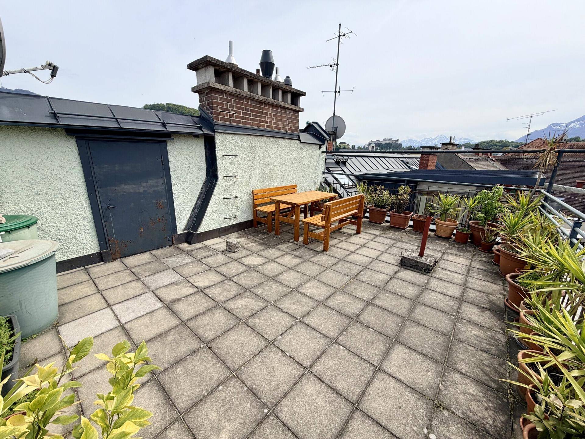 Dachterrasse mit Sitzgelegenheiten, Pflanzen und weitem Blick über die Dächer der Stadt.