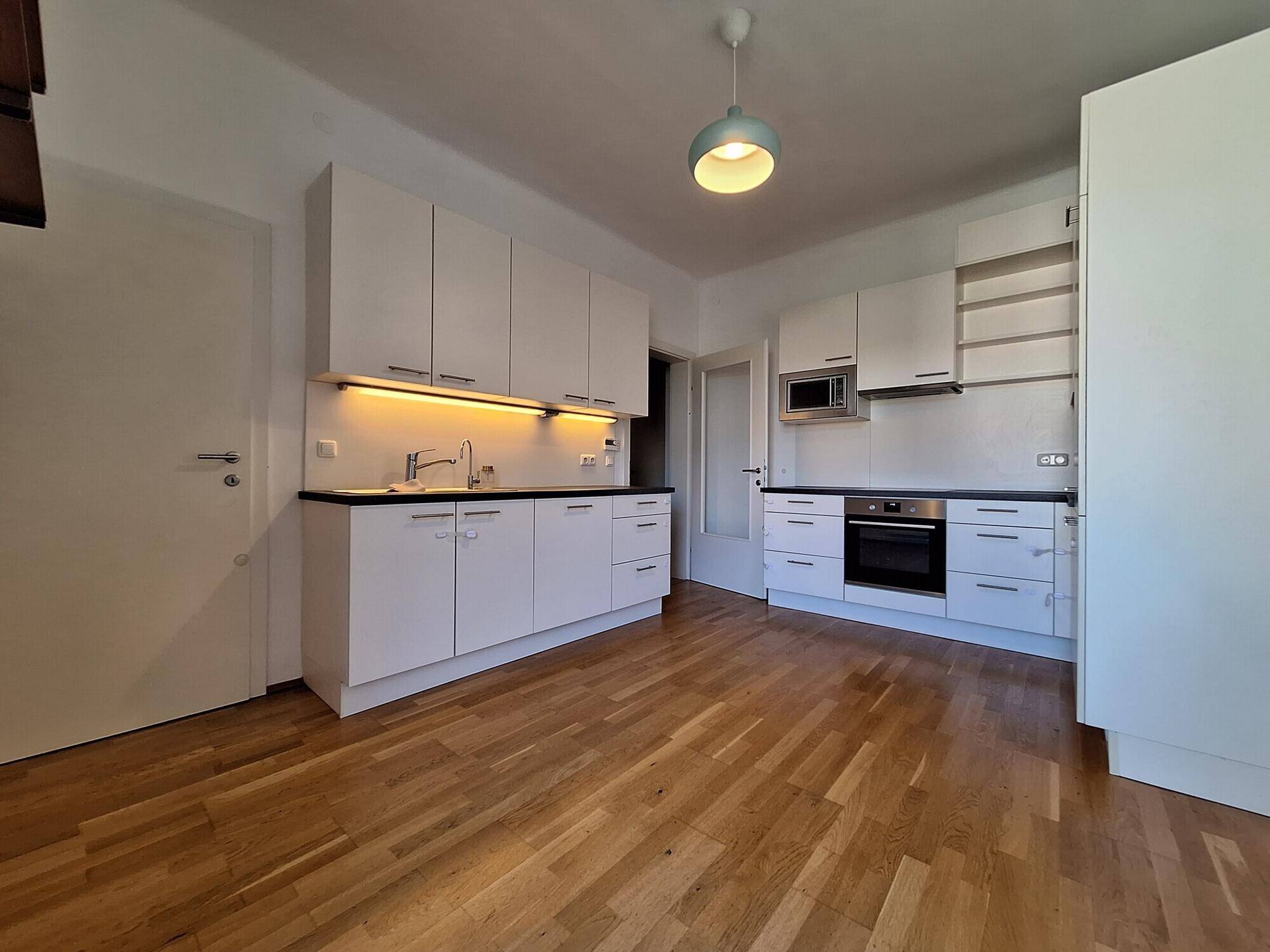 Moderne Einbauküche mit weißen Schränken, dunkler Arbeitsplatte und integrierten Geräten.