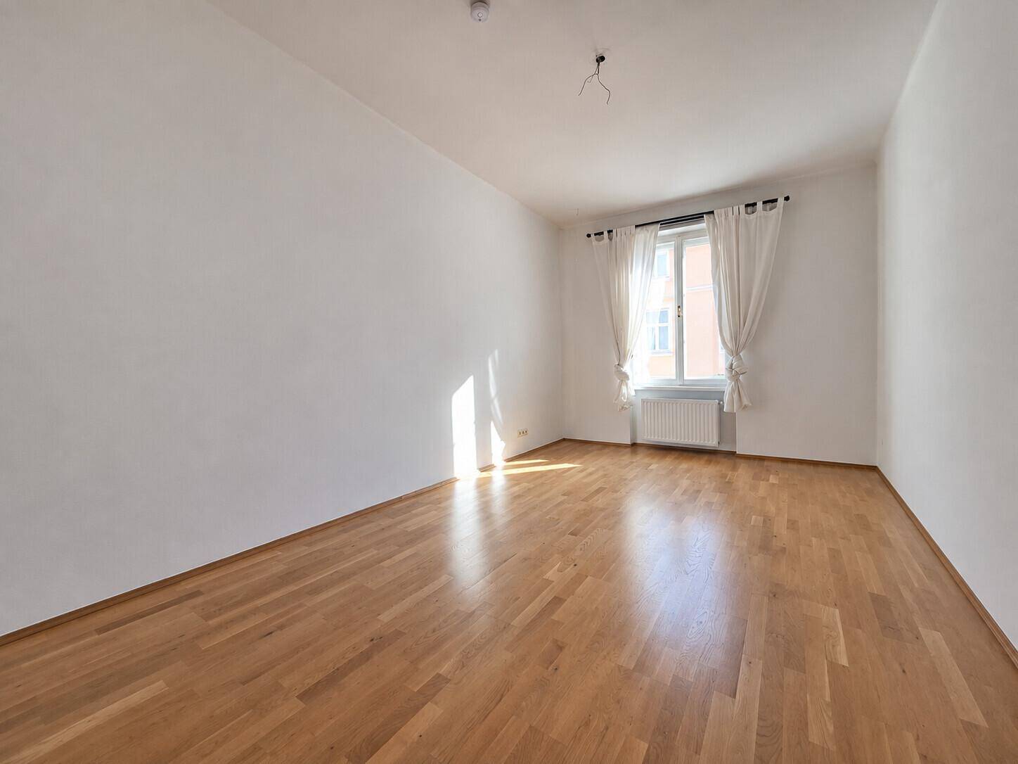 Helles Wohnzimmer mit Parkettboden und viel Sonneneinstrahlung durch das Fenster, einladend.