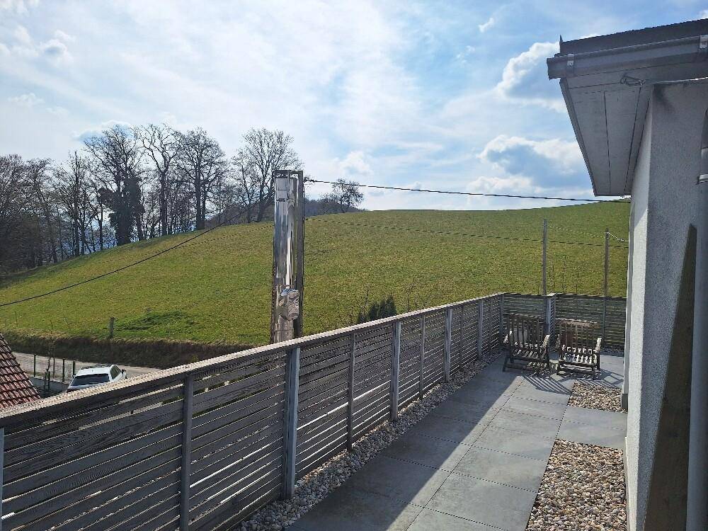 Geräumige Terrasse mit Holzzaun, Kies und weitem Blick auf die umliegende grüne Landschaft.