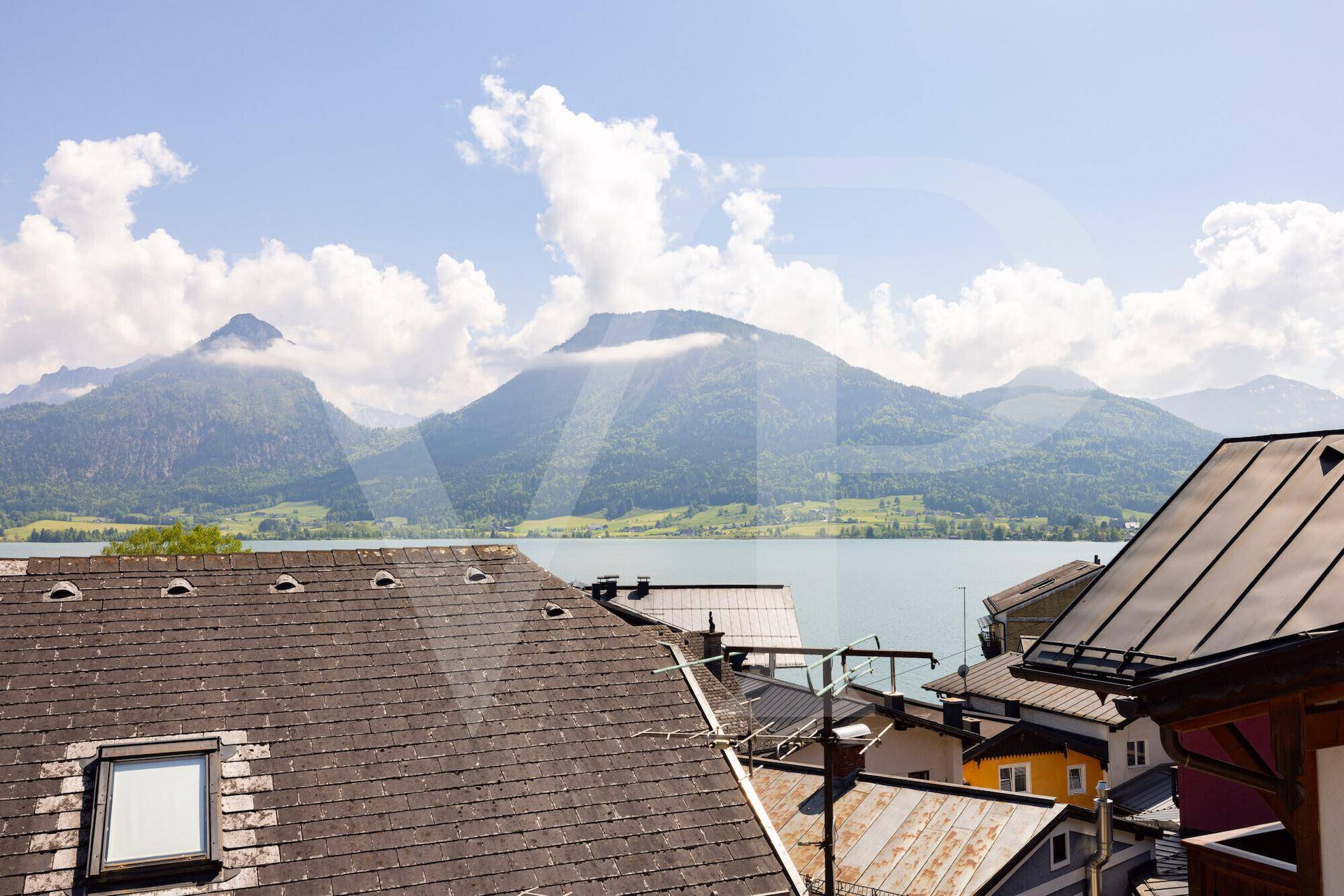 Weitläufiger Ausblick auf einen See und die majestätischen Berge, umrahmt von Dächern.