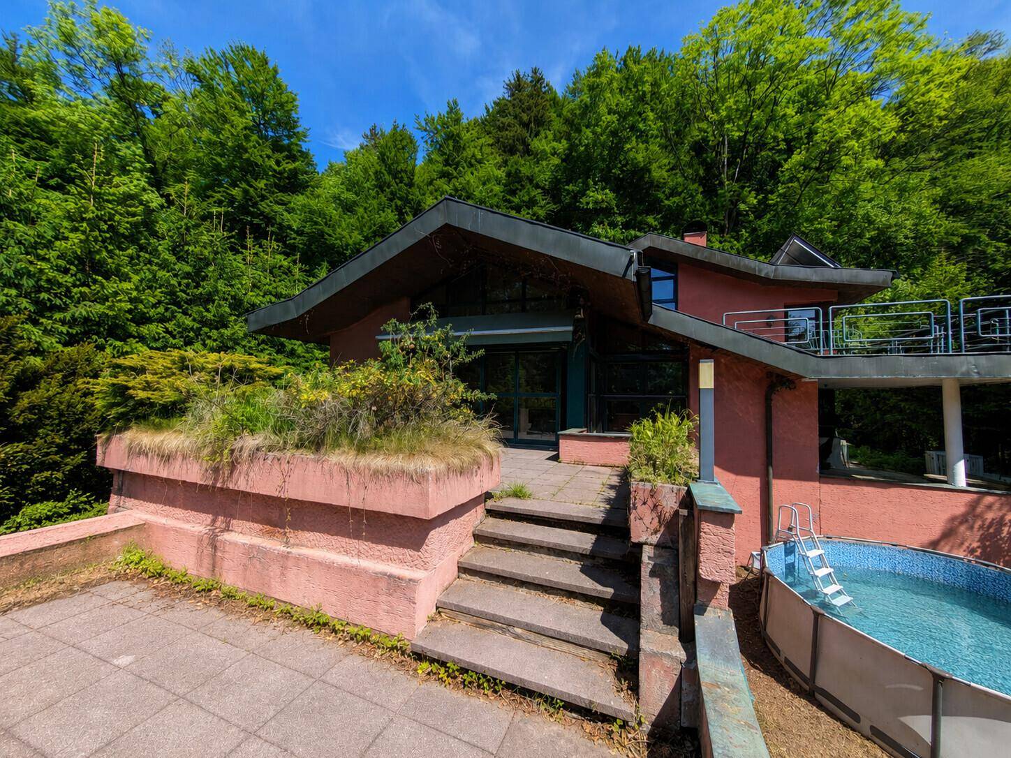 Terrasse mit Steinstufen, angrenzendem Haus und einem Aufstellpool im Gartenbereich.