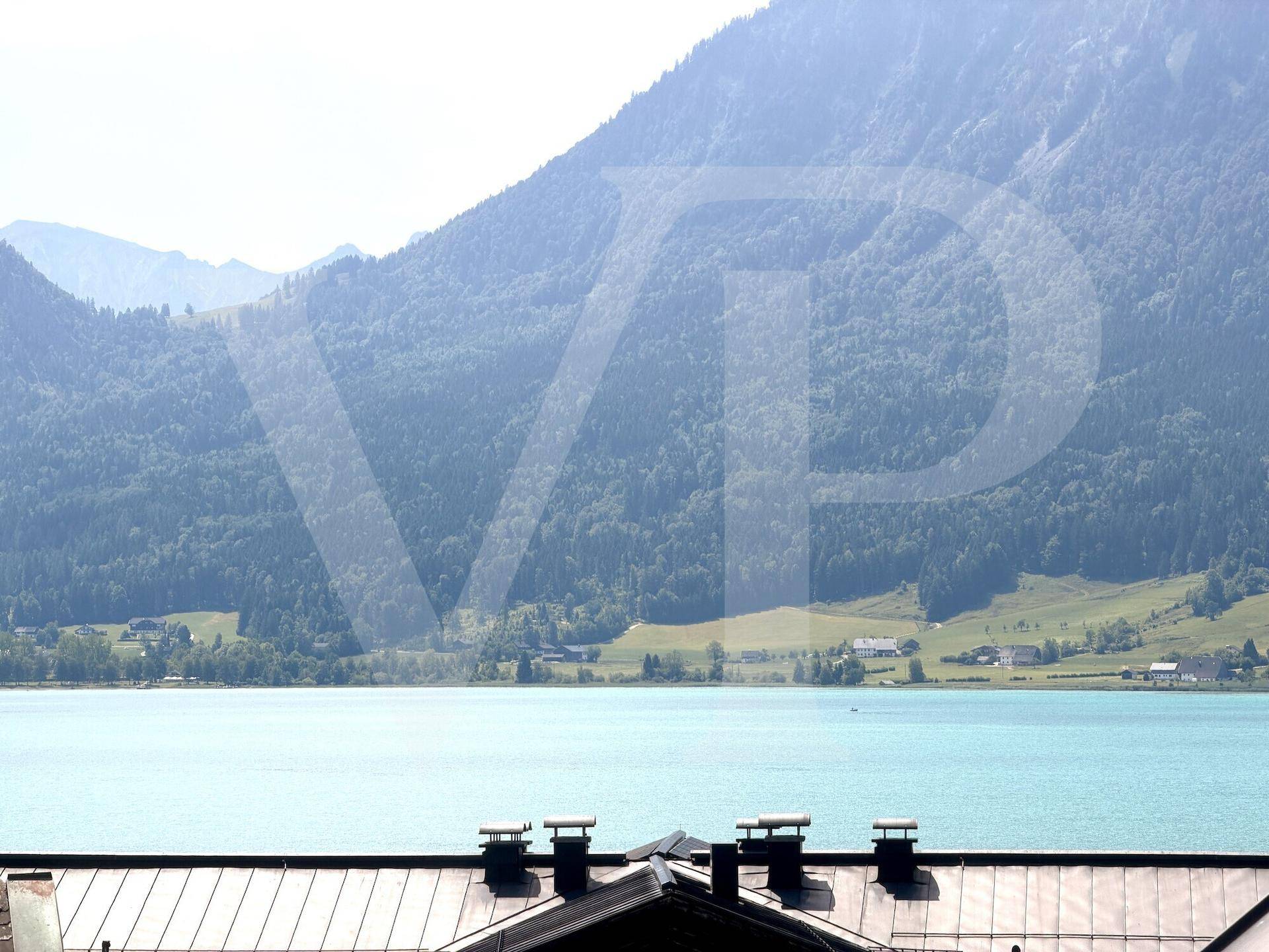 Malerischer Blick auf einen See und die umliegenden Berge über den Dächern der Häuser.