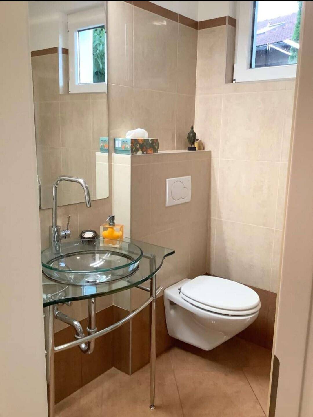 Modernes Gäste-WC mit Wand-WC, stilvollem Glaswaschbecken und beigefarbenen Fliesen.